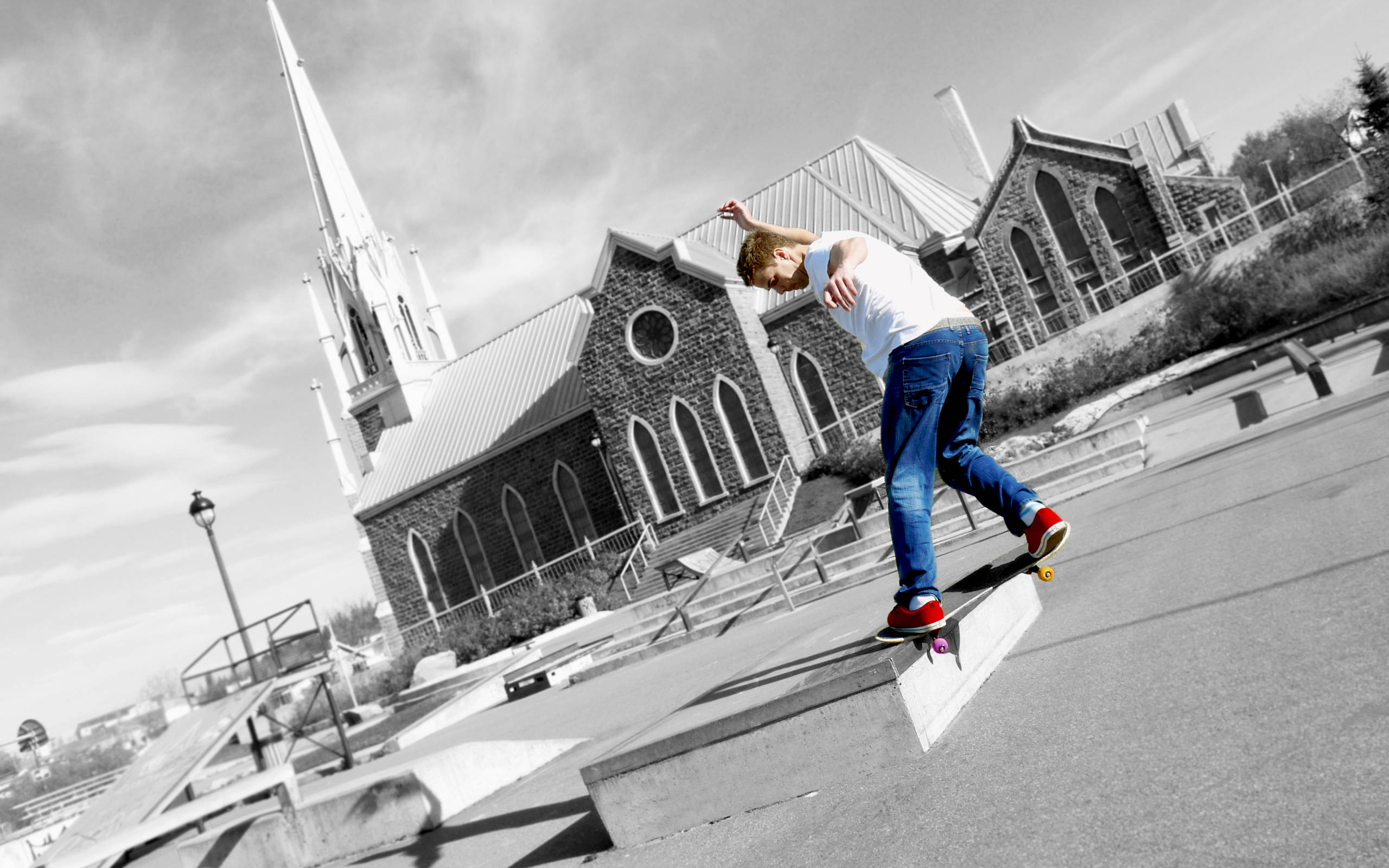 Skater Boy 桌布 壁紙 — 一名身穿白色T恤和藍色牛仔褲的滑板手，穿著紅色鞋子，在哥德式教堂的黑白背景下磨滑混凝土邊緣。
