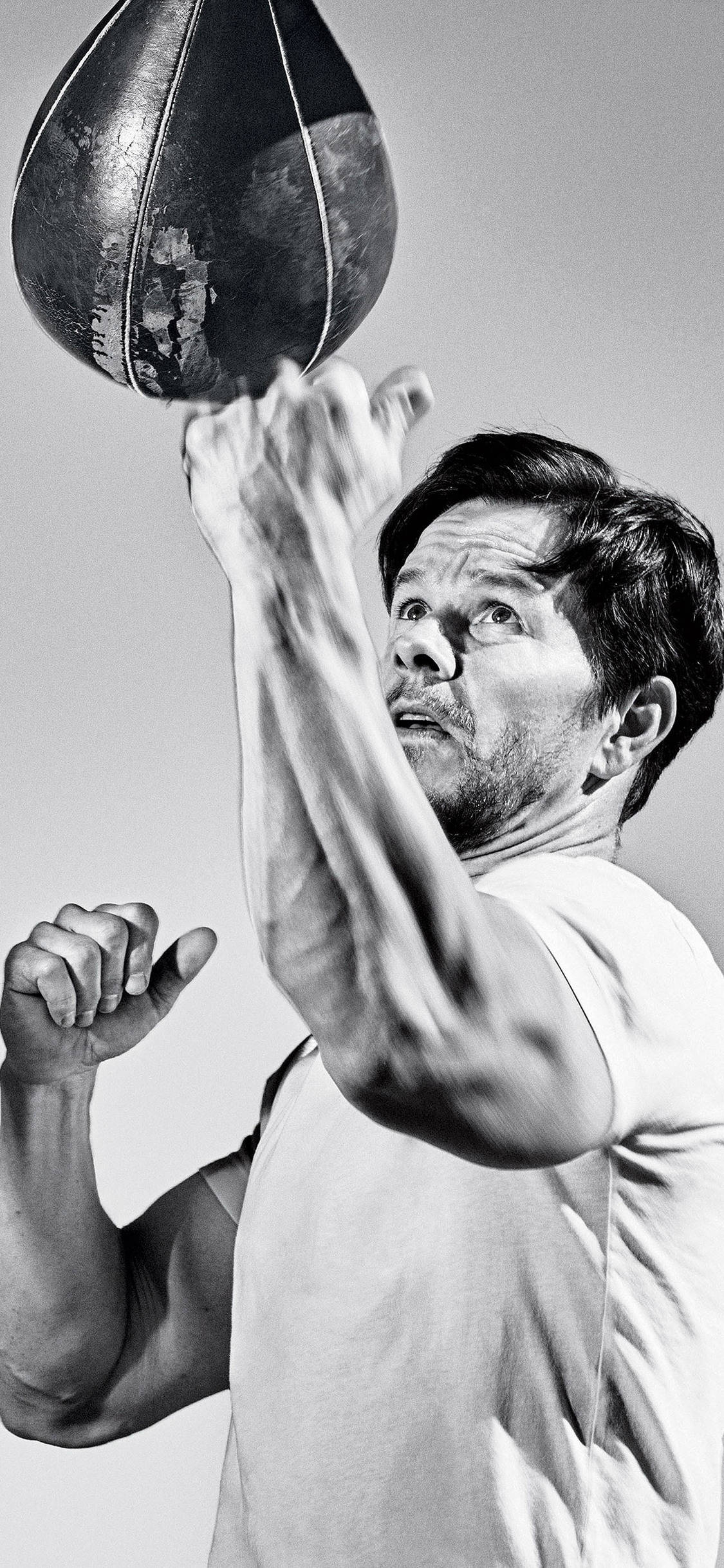 Mark Wahlberg 桌布 壁紙 — 一名身穿白色T恤的男子在清晰的黑白工作室照片中猛烈地擊打一個破舊的皮革拳擊沙包。