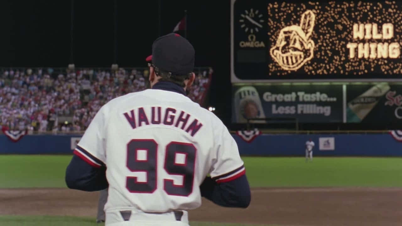 Major League Movie 桌布 壁紙 — 一名身穿白色Vaughn 99球衣的棒球運動員在夜間站在球場上，面向發光的記分板，上面寫著「WILD THING」，背景有觀眾。