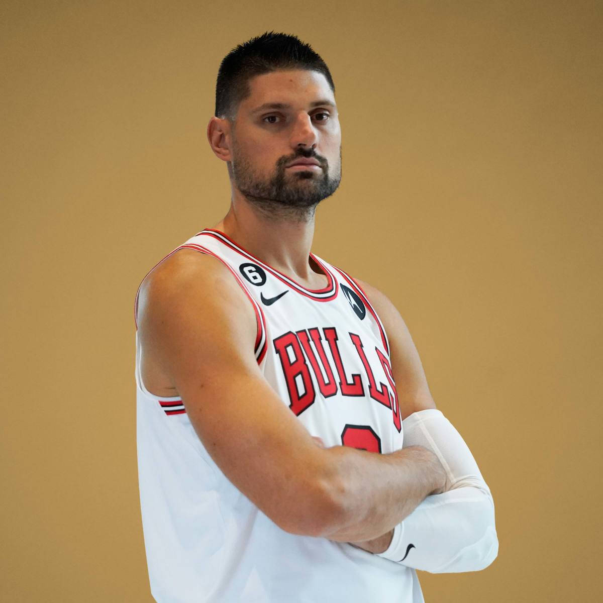 NBA 桌布 壁紙 — 一名身穿白色公牛隊球衣的籃球運動員，在純色米色背景前自信地交叉雙臂站立。