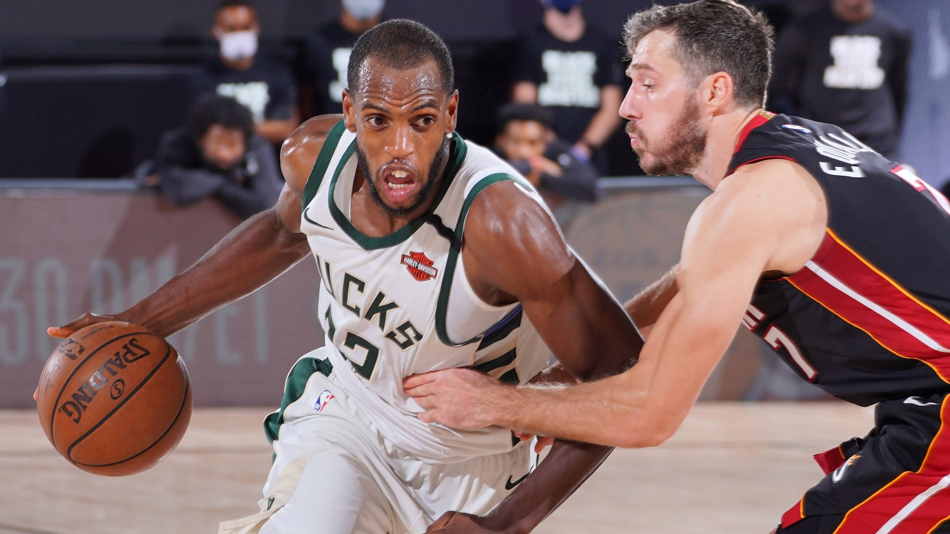 Khris Middleton 桌布 壁紙 — 一名身穿白色公鹿球衣的籃球運動員在激烈的比賽中突破身穿黑紅球衣的防守球員。
