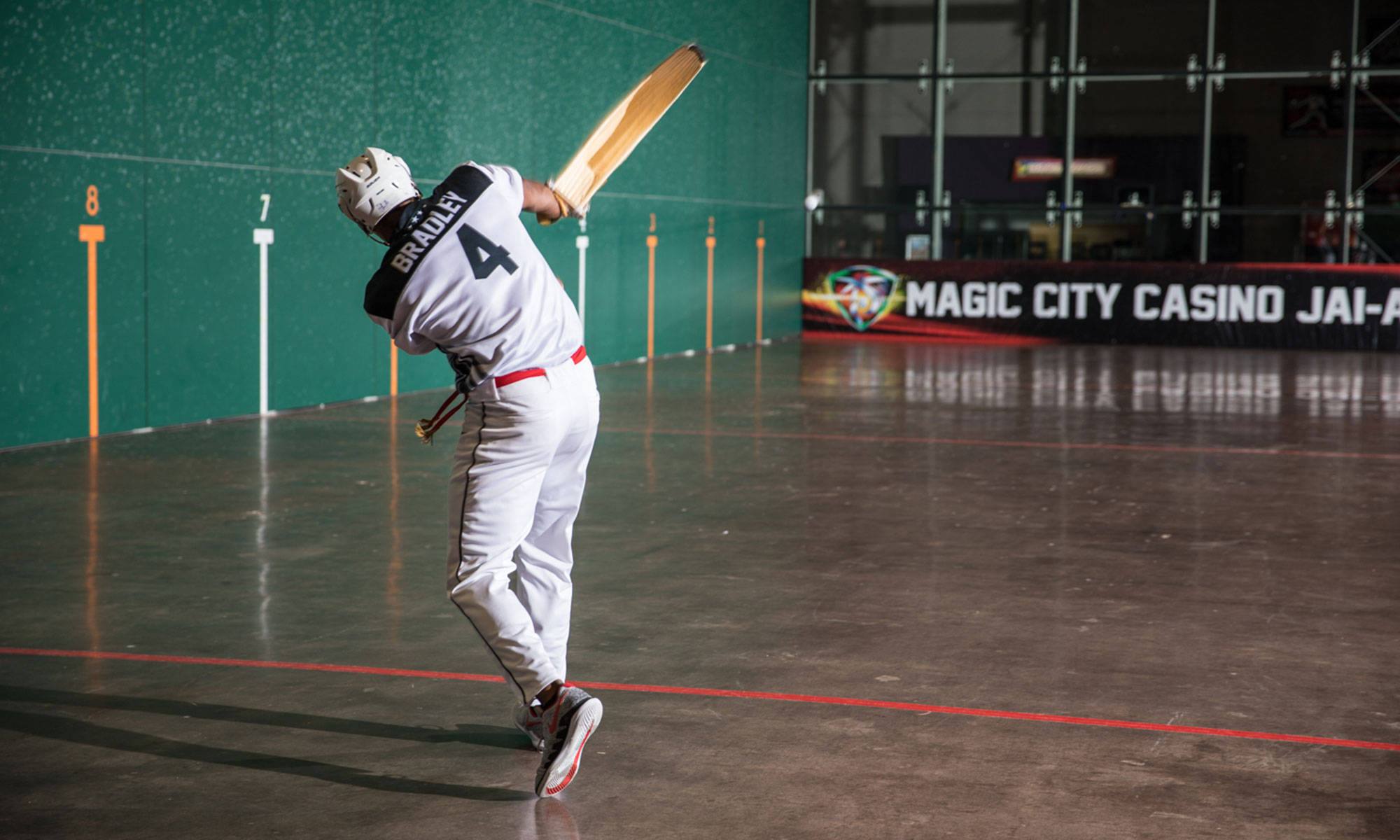 Athletic 桌布 壁紙 — 一名身穿白色制服的球員在室內球場揮動壁球拍，牆壁為綠色，並有「Magic City Casino」橫幅。