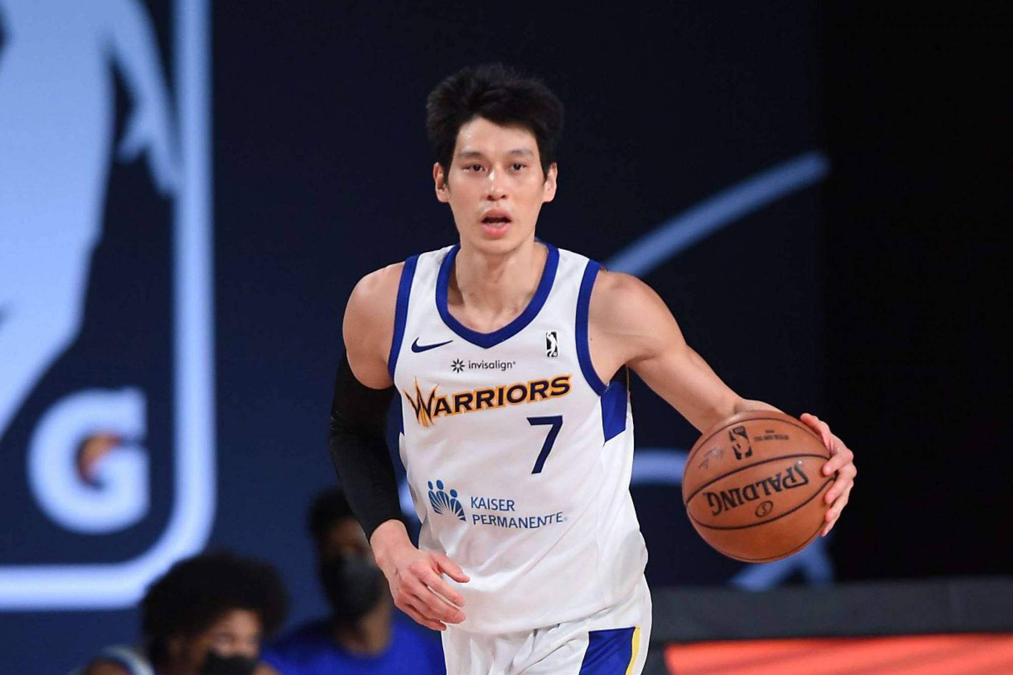 Lin 桌布 壁紙 — 一名身穿白色勇士隊球衣的籃球運動員在明亮的場館燈光下，於比賽中專注地運球。