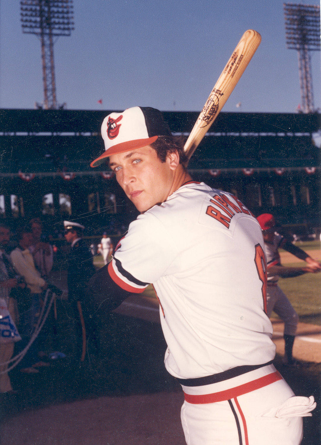 cal ripken jr 桌布 壁紙 — 一名身穿白色和橙色球衣的棒球運動員在明亮的日光下，於球場上將球棒扛在肩上。
