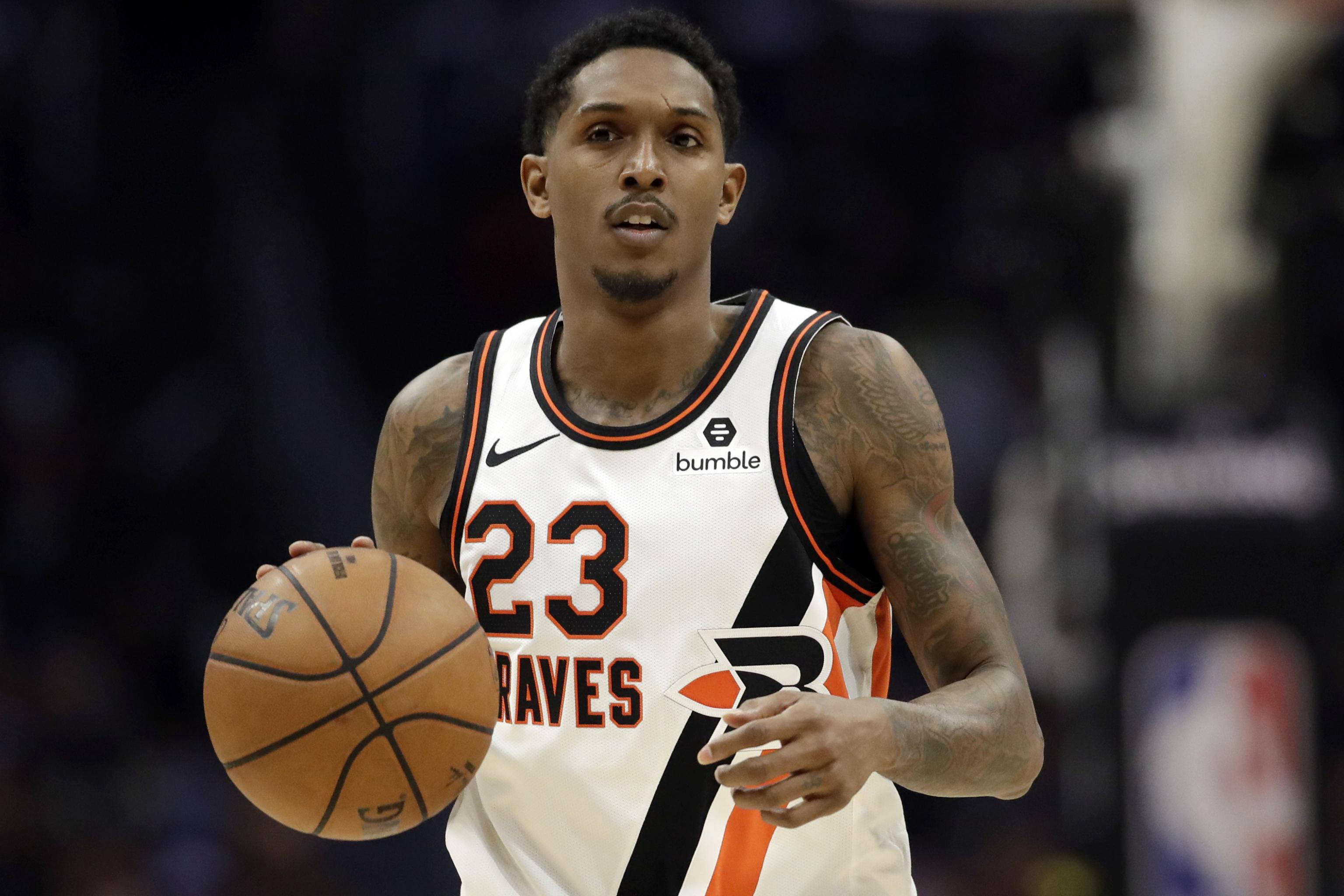 Lou Williams 桌布 壁紙 — 一名身穿白色和橙色球衣的籃球運動員在比賽中，在場館燈光下專注地持球。