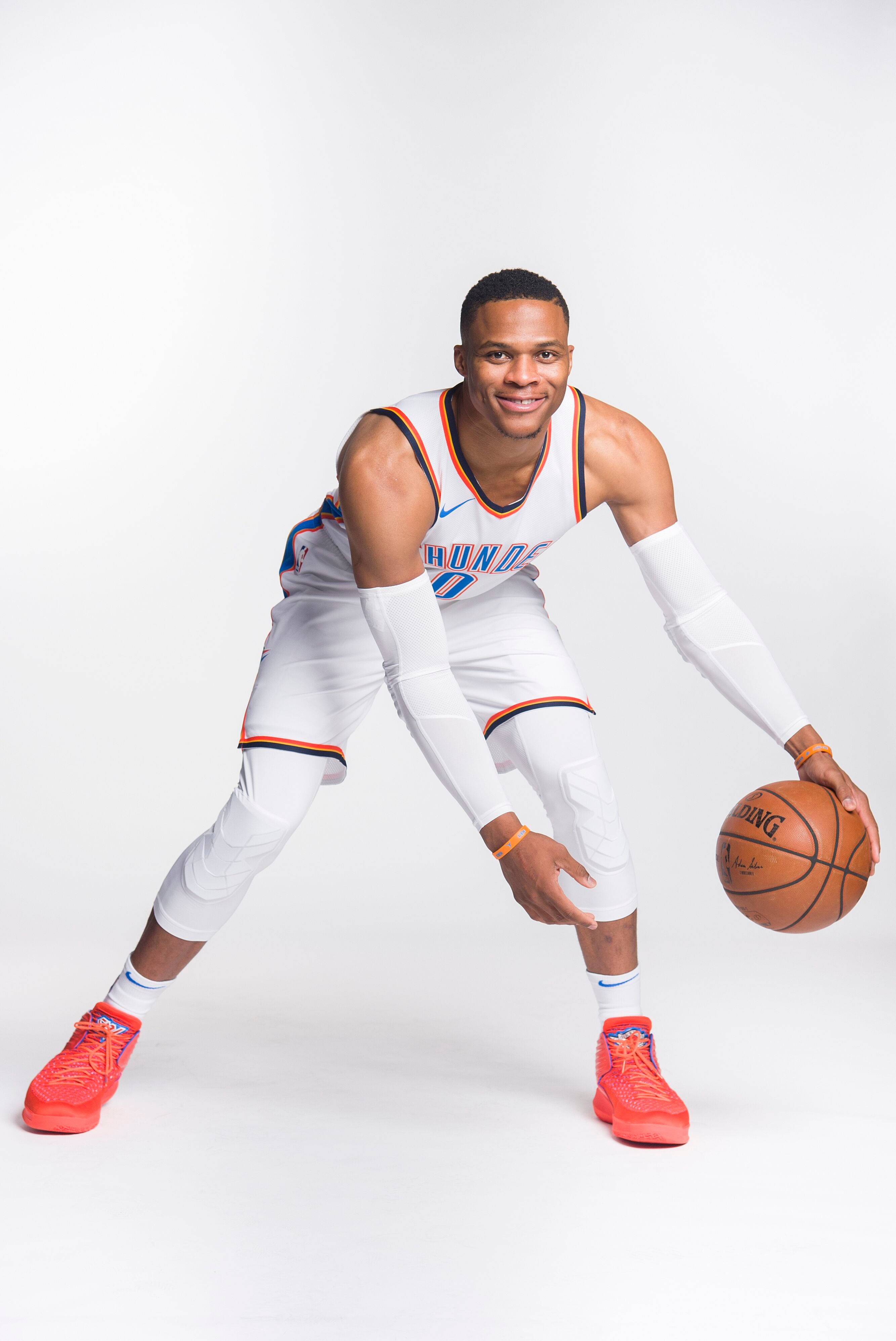 Westbrook 桌布 壁紙 — 一名身穿白色和橙色球衣的籃球運動員在純白色背景前運球微笑。