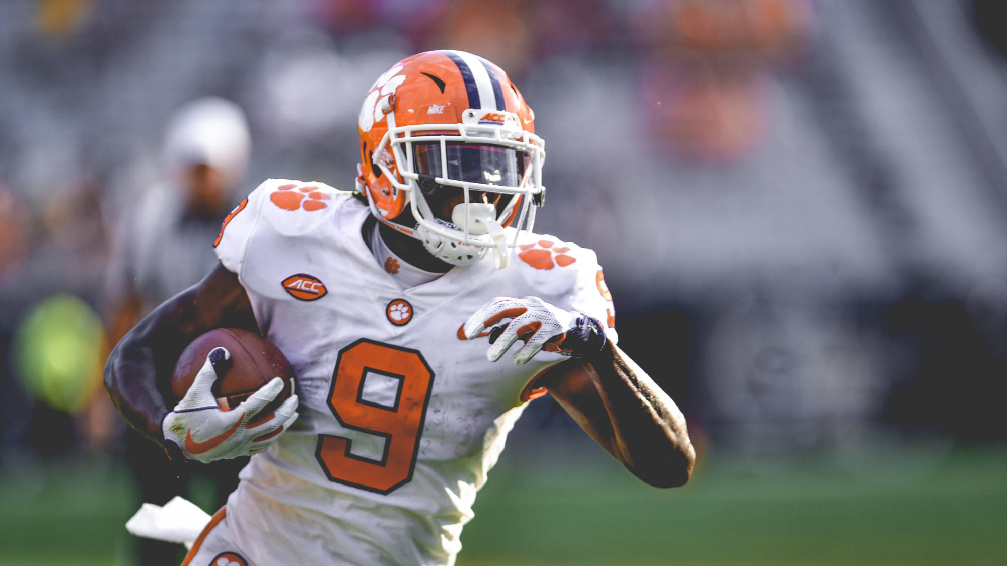 Travis Etienne 桌布 壁紙 — 一名身穿白色和橙色裝備的克萊姆森美式足球員在日間比賽中持球衝刺。
