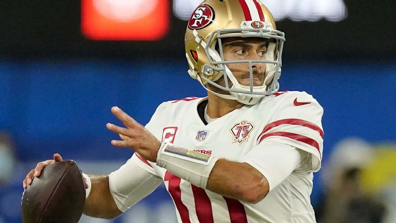 Jimmy Garoppolo 桌布 壁紙 — 一名身穿白色和紅色球衣的舊金山四九人四分衛在夜間比賽中，在球場燈光下準備擲出橄欖球。
