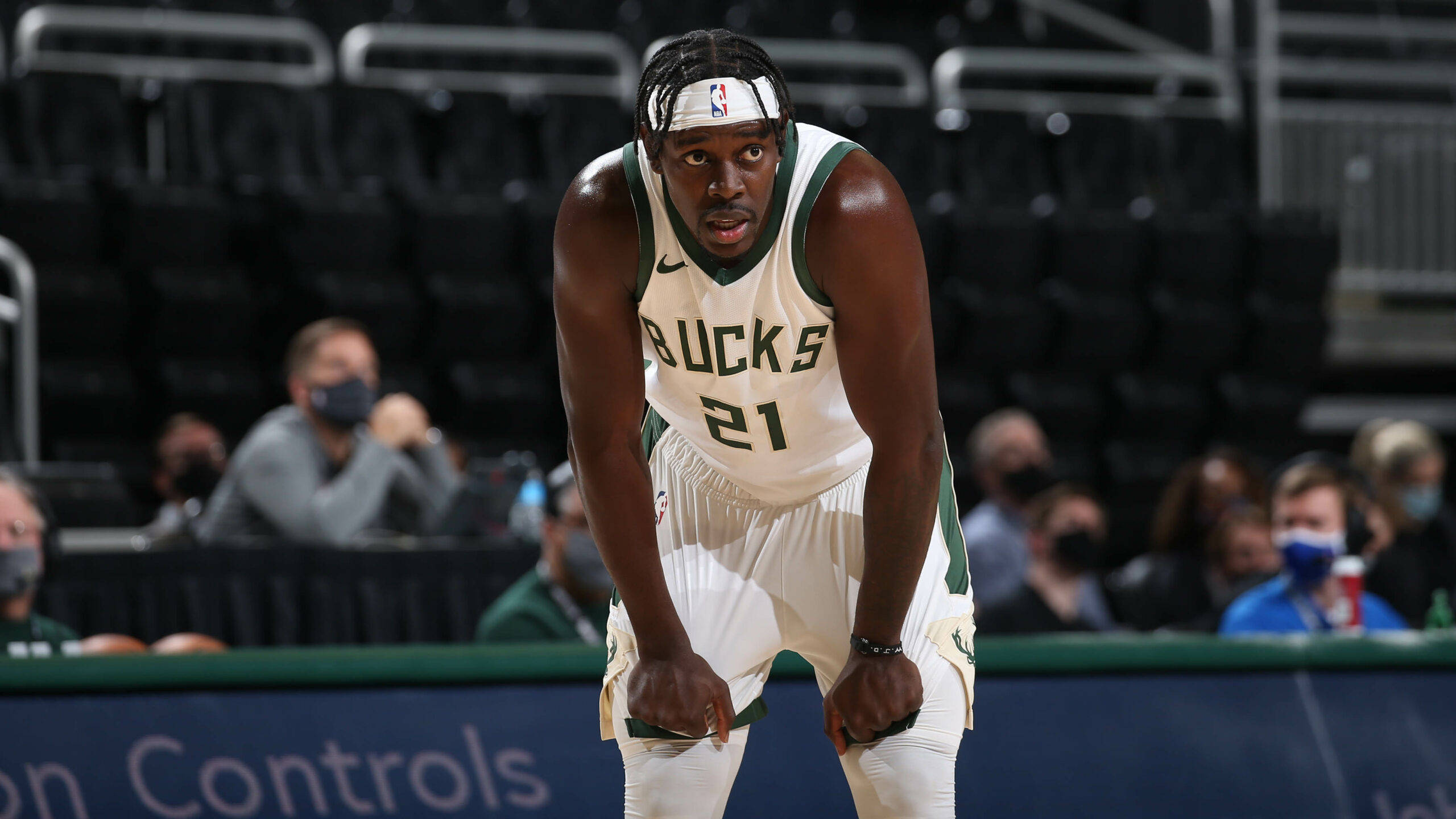 Jrue Holiday 桌布 壁紙 — 一名身穿白色和綠色球衣的密爾瓦基公鹿籃球運動員在球場上激烈前傾，背景有戴口罩的觀眾。