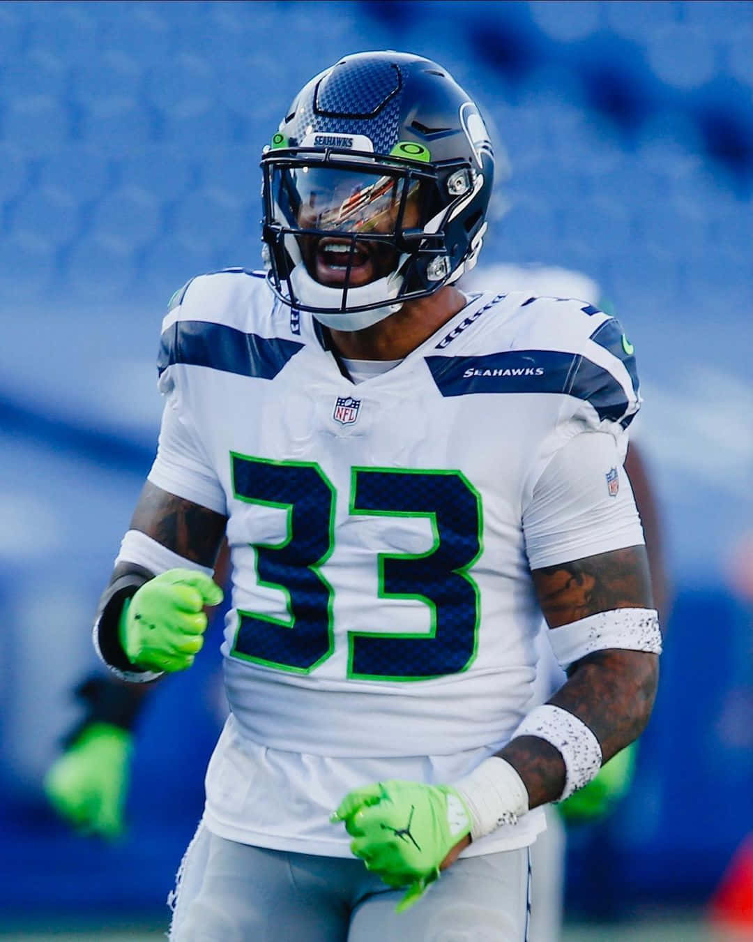 Seattle Seahawks 桌布 壁紙 — 一名身穿白色和綠色球衣的西雅圖海鷹隊美式足球運動員在藍色球場上激烈奔跑。