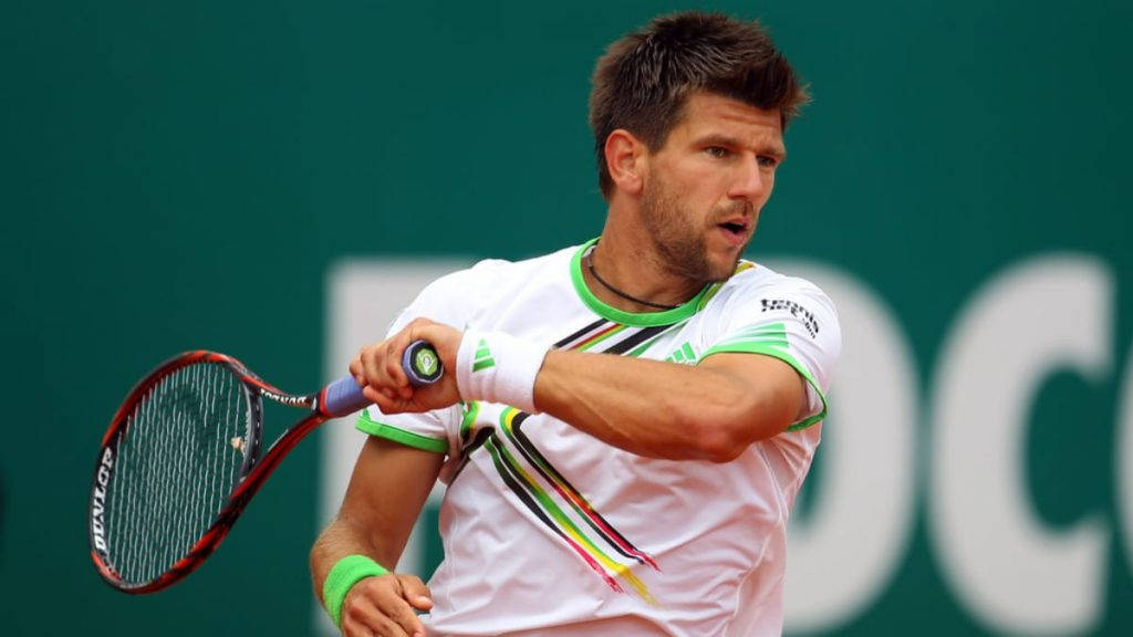 Tennis 桌布 壁紙 — 一名身穿白色和綠色裝備的男性網球選手，在綠色球場背景下，專注地揮動紅色球拍。