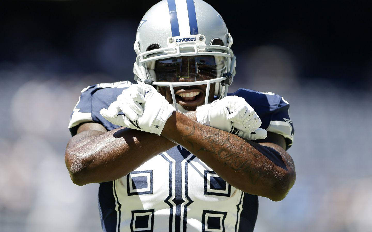 NFL Players 桌布 壁紙 — 一名身穿白色和藍色制服的達拉斯牛仔隊美式足球員，戴著頭盔和手套，交叉雙臂，露出燦爛笑容。