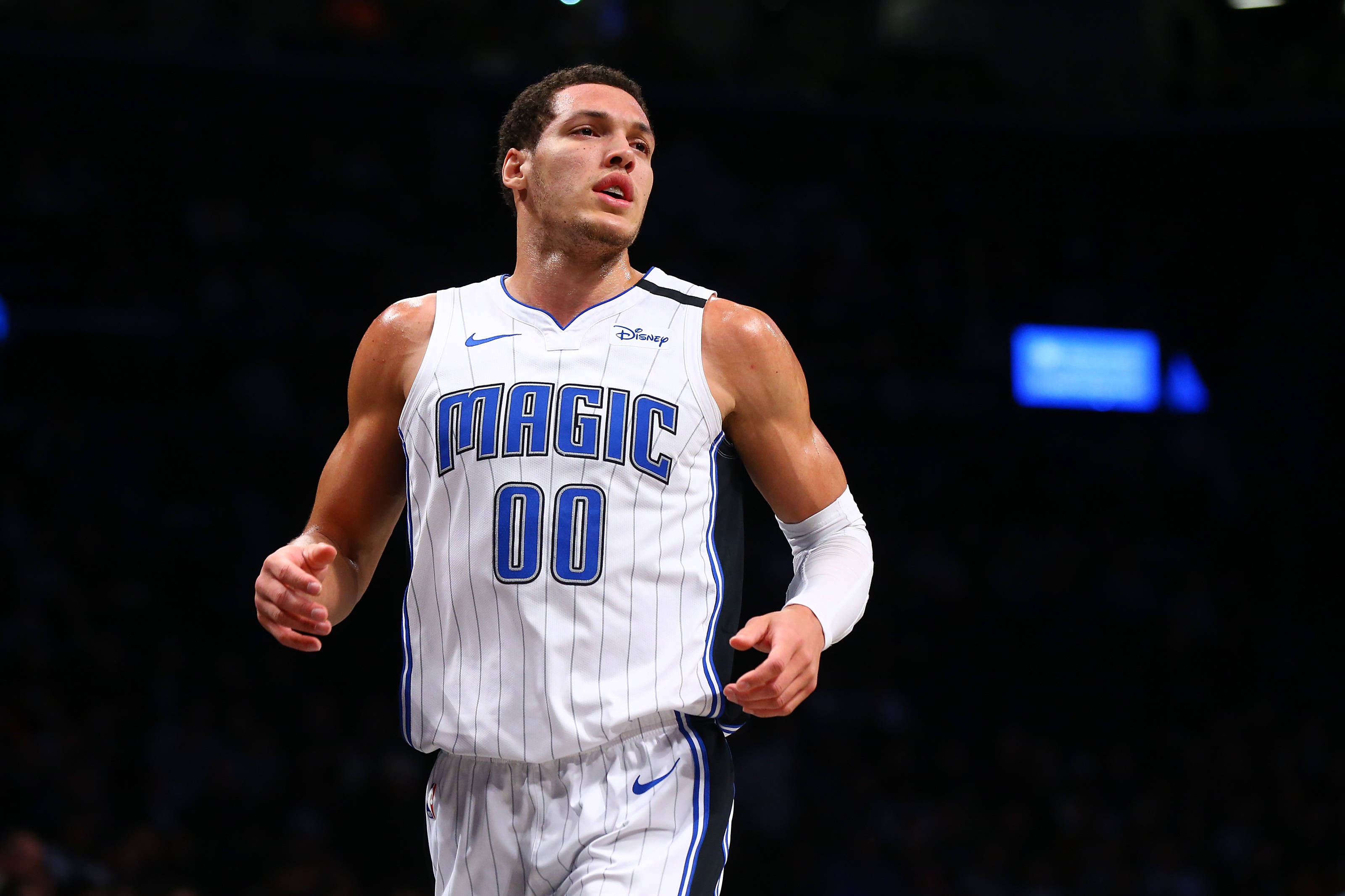 aaron gordon 桌布 壁紙 — 一名身穿白色和藍色奧蘭多魔術隊球衣、背號00的籃球運動員在明亮的場館燈光下於比賽中激烈奔跑。