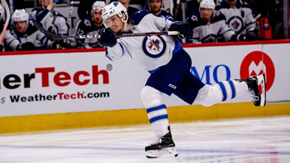 hockey 桌布 壁紙 — 一名身穿白色和藍色球衣的冰球運動員在比賽中動態地在冰上滑行，球桿高舉。