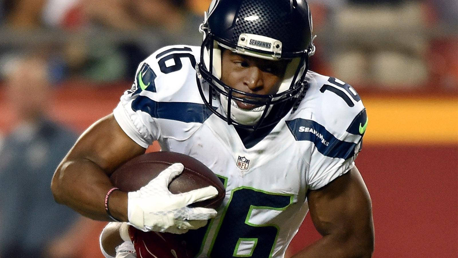 Seattle Seahawks 桌布 壁紙 — 一名身穿白色和藍色球衣的西雅圖海鷹隊美式足球員在夜間比賽中，在球場燈光下帶球奔跑。