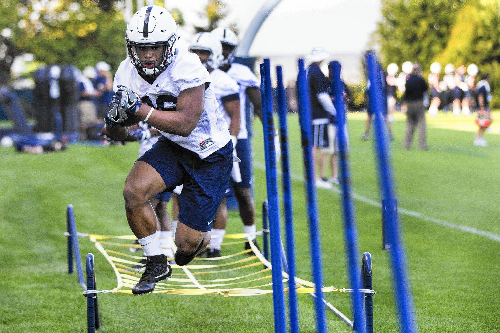 Saquon Barkley 桌布 壁紙 — 一名身穿白色和藍色裝備的足球運動員在白天訓練期間在草地上衝過藍色敏捷桿。