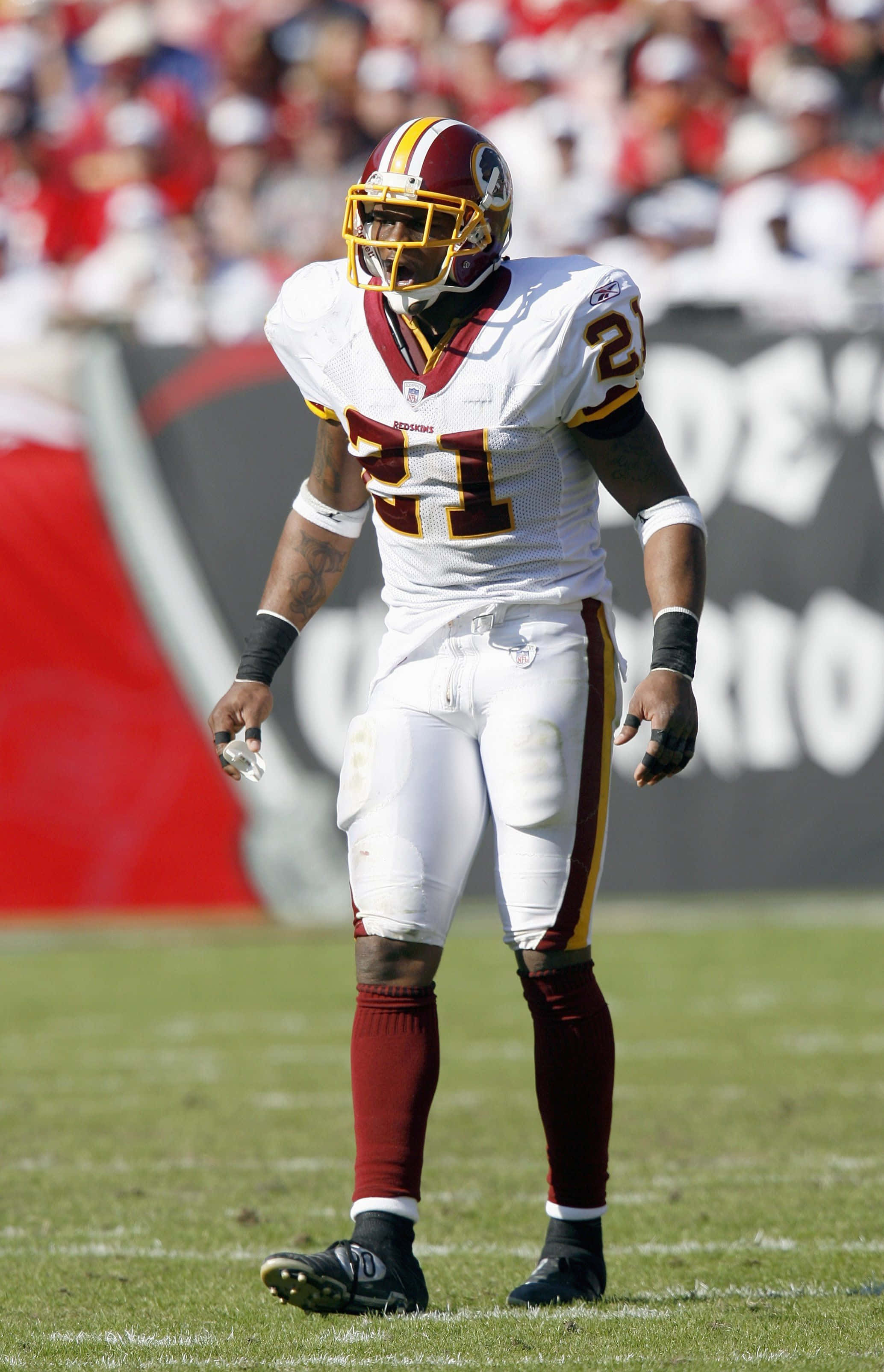 Sean Taylor 桌布 壁紙 — 一名身穿白色和酒紅色球衣的華盛頓紅皮隊美式足球員，站在陽光普照的綠色球場上，背景是模糊的體育場觀眾。