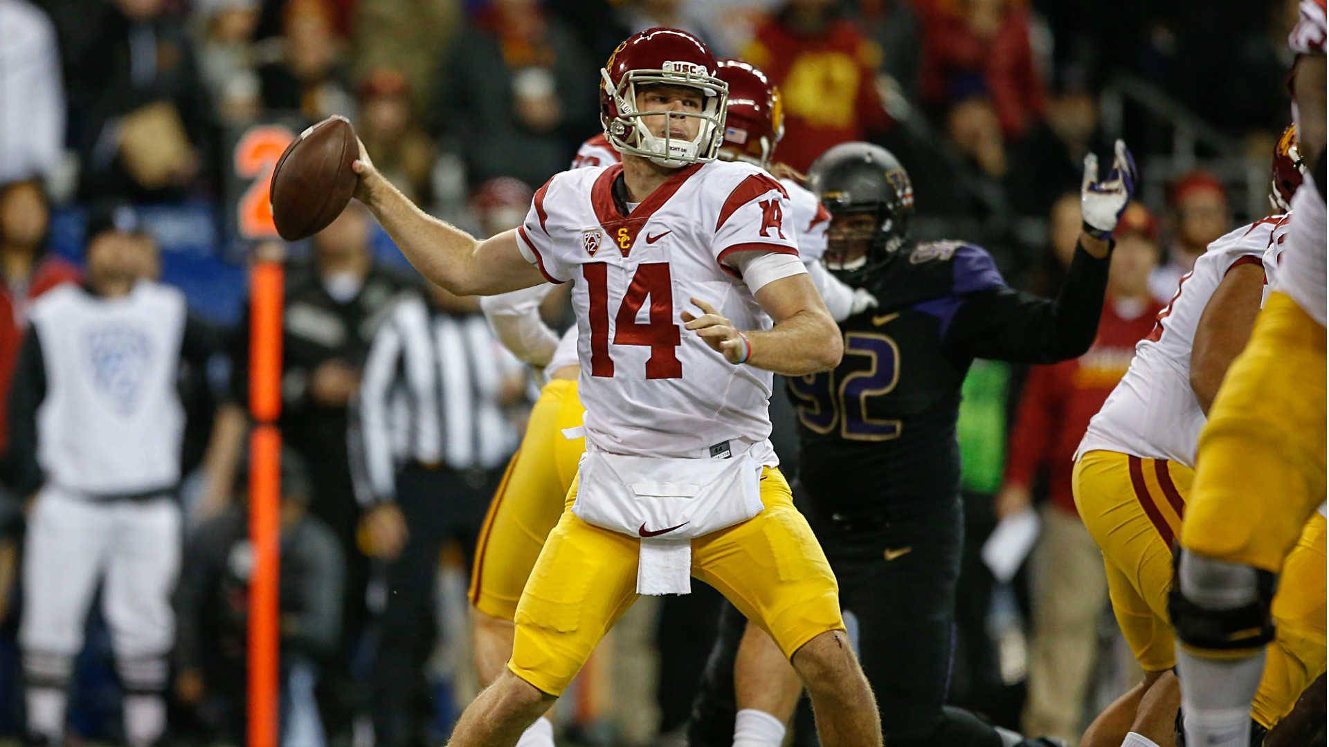 Football Players 桌布 壁紙 — 一名身穿白色和金色制服的大學美式足球四分衛在體育場燈光下的夜間比賽中擲球。
