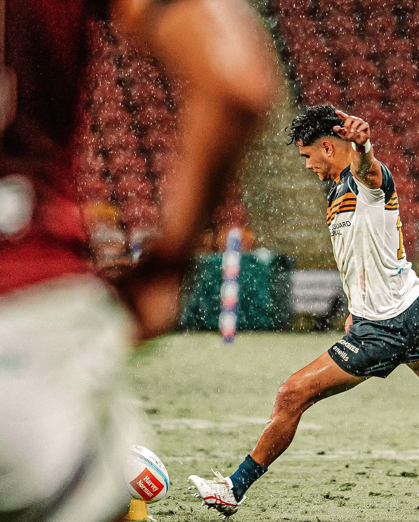 Brumbies 桌布 壁紙 — 一名身穿白色和金色球衣的橄欖球運動員在傾盆大雨中踢球，空氣中懸浮著水滴。