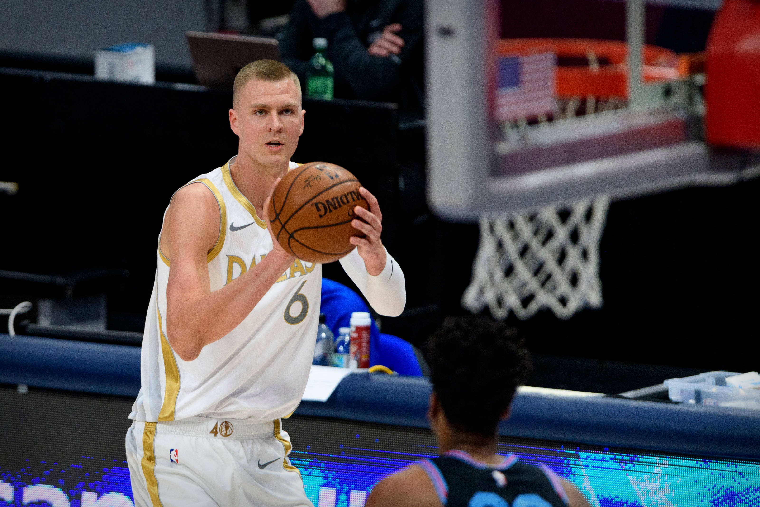 Kristaps Porzingis 桌布 壁紙 — 一名身穿白色和金色球衣的籃球運動員在籃框附近被對手防守，準備投籃。