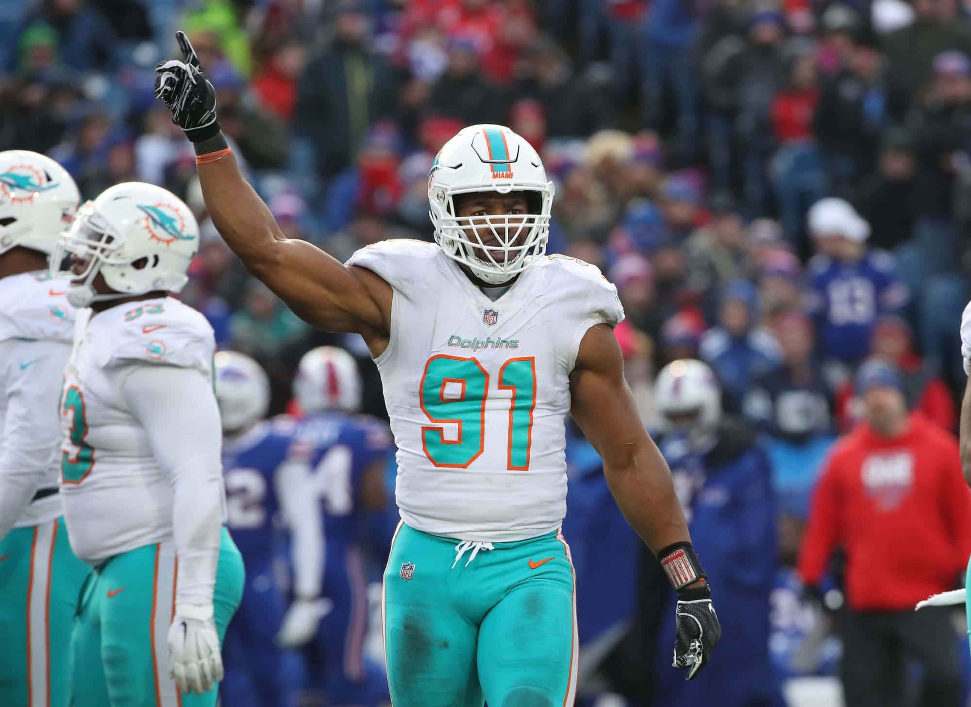 足球 桌布 壁紙 — 一名身穿白色和青色球衣的邁阿密海豚隊美式足球員在比賽中於球場上勝利地舉起拳頭。