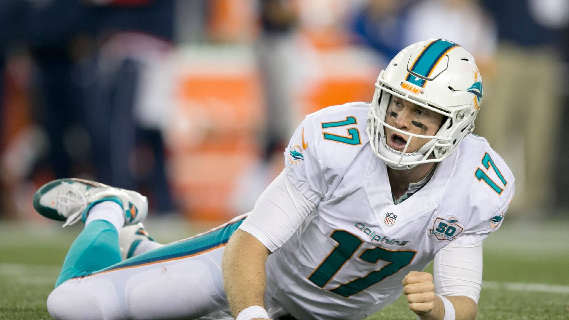 dolphins 桌布 壁紙 — 一名身穿白色和青色球衣的邁阿密海豚四分衛在比賽中躺在草地上，表情專注。