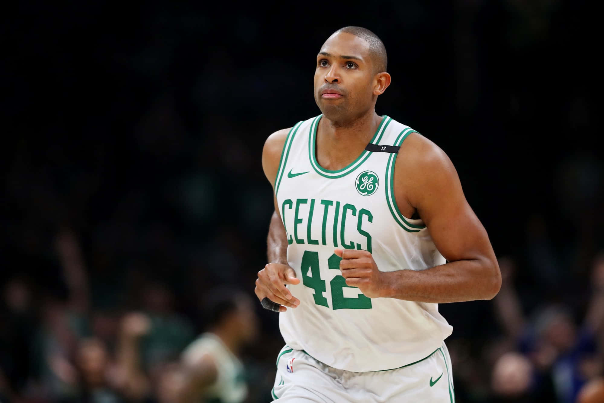 Al Horford 桌布 壁紙 — 一名身穿白色塞爾提克球衣、背號42的籃球運動員在明亮的場館燈光下專注地奔跑比賽。