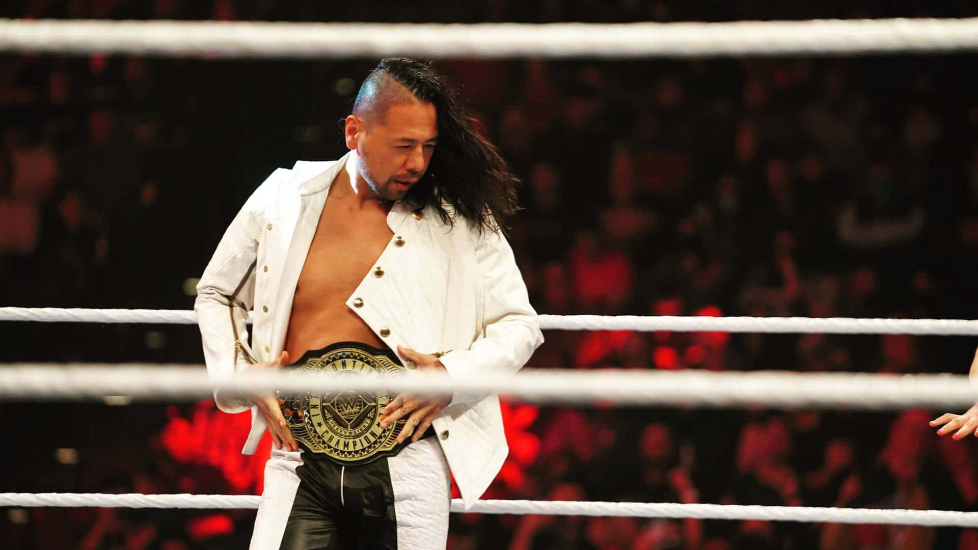 WWE 桌布 壁紙 — 一名身穿白色外套的摔角手在燈光明亮的擂台上高舉冠軍腰帶，身後是模糊的人群。