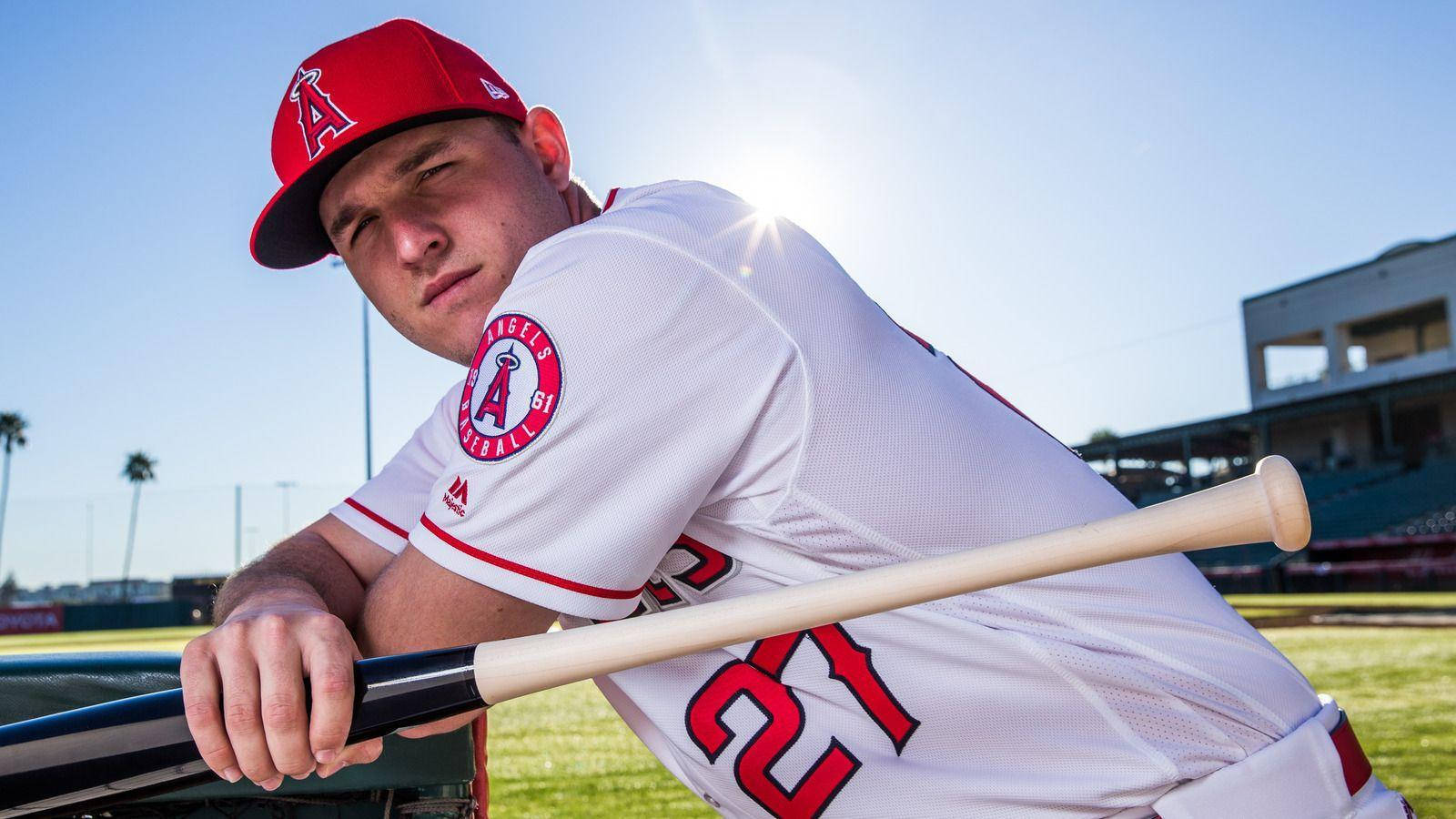 Mike Trout 桌布 壁紙 — 一名身穿白色天使隊球衣的棒球運動員在明亮的陽光下，以棕櫚樹和球場為背景，靠在球棒上。