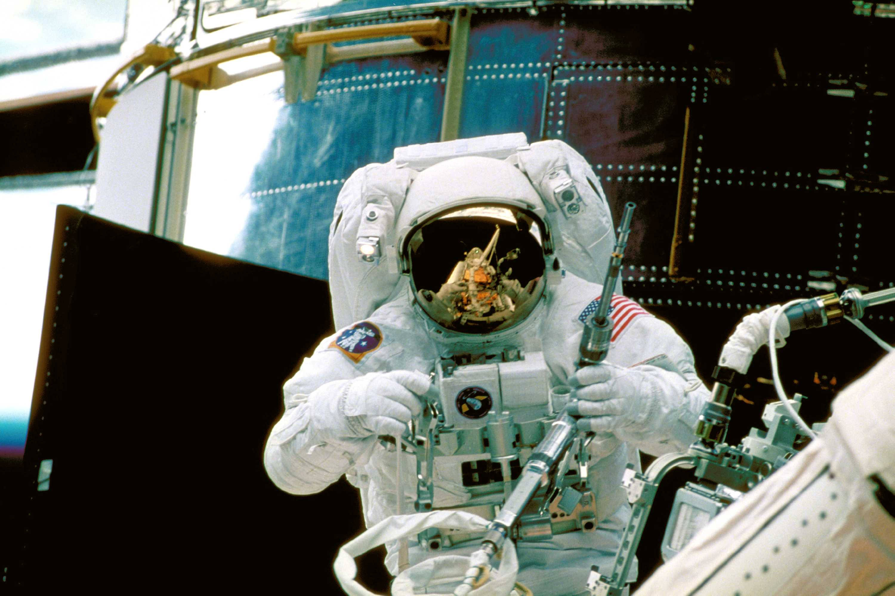 nasa 美學 桌布 壁紙 — 一名身穿白色太空衣的太空人在太空船外進行太空漫步，頭盔反射中可見地球。