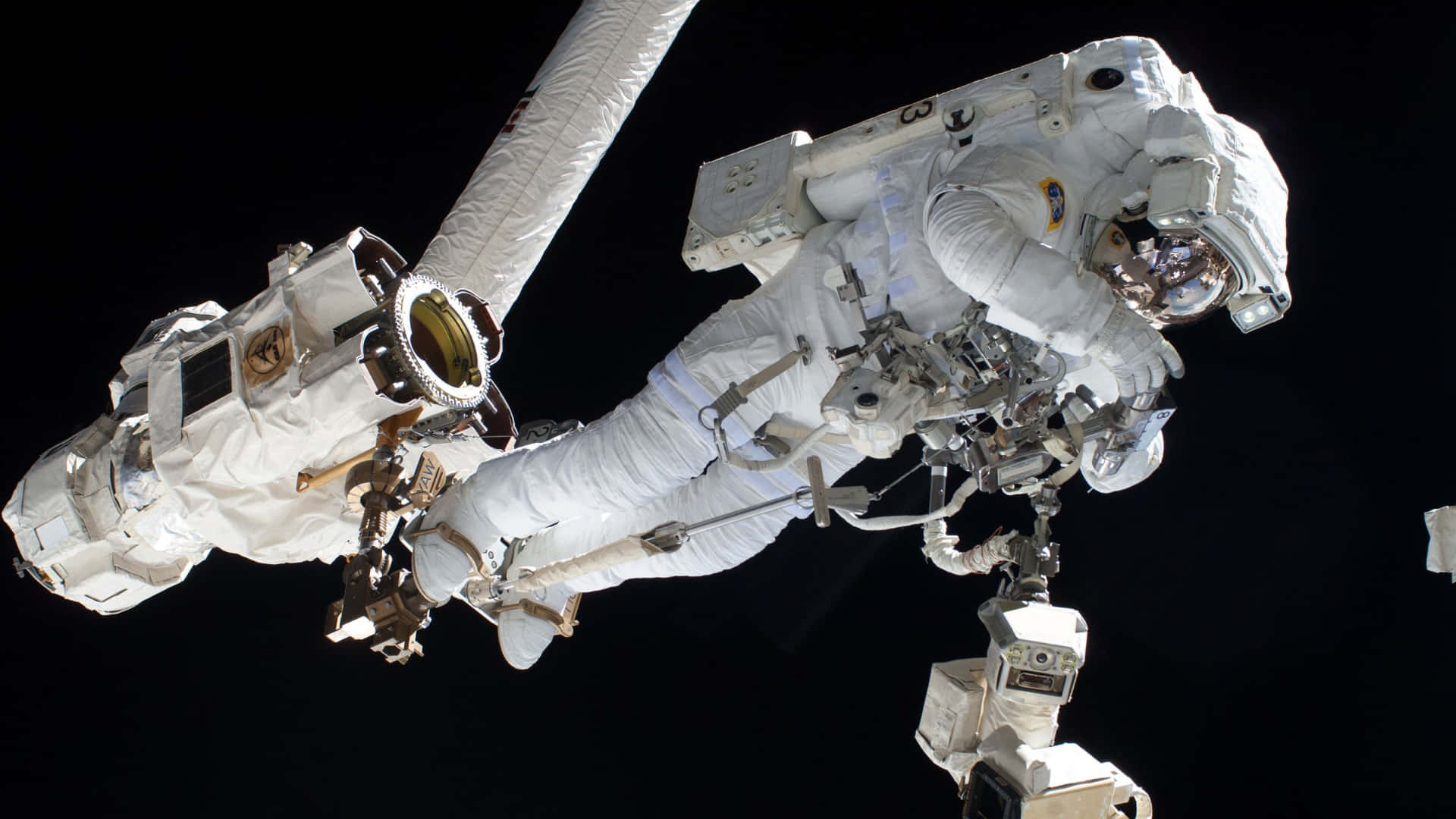 Space Mission 桌布 壁紙 — 一名身穿白色太空衣的太空人在漆黑的太空中，於國際太空站外進行太空漫步。