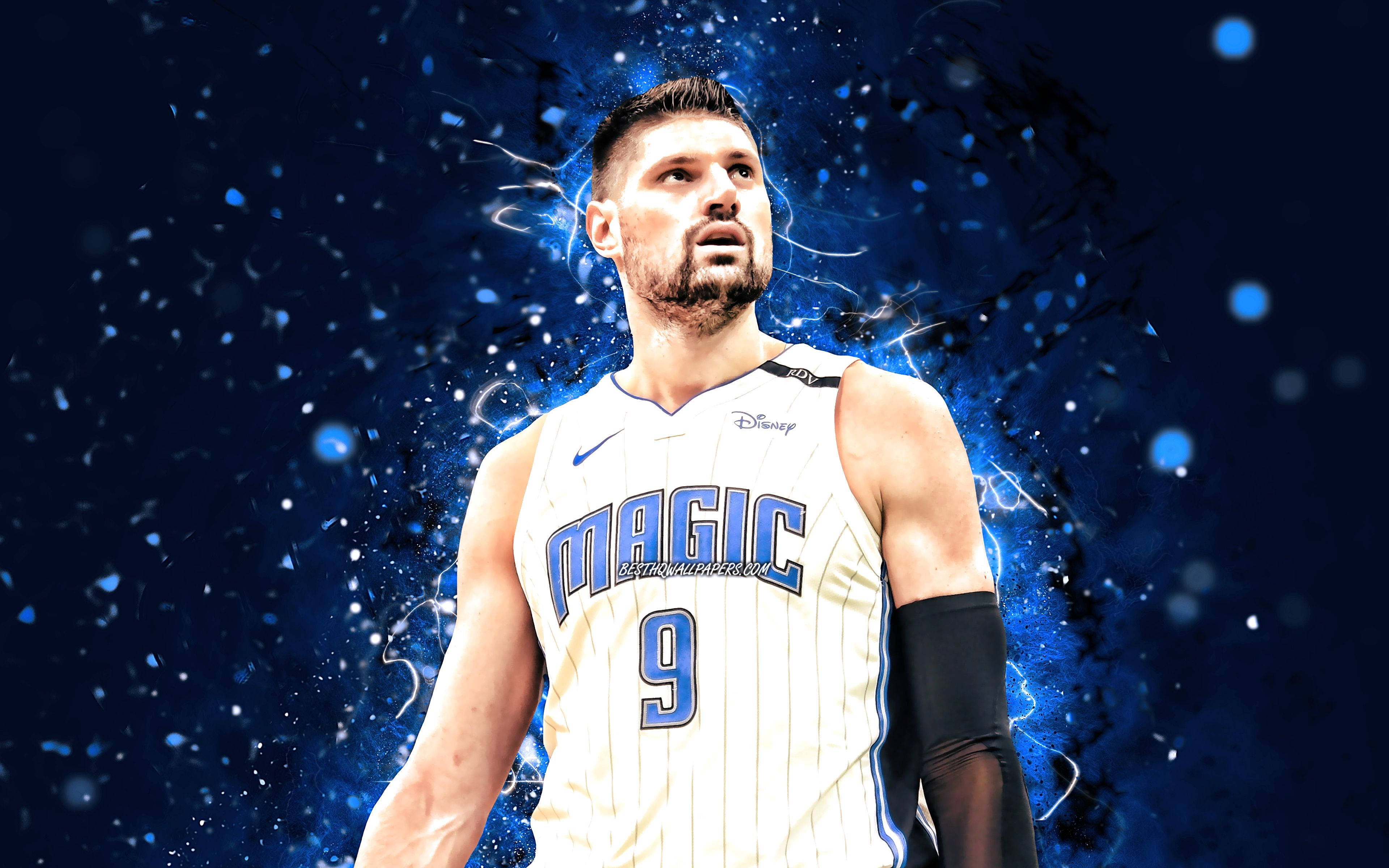 NBA 桌布 壁紙 — 一名身穿白色奧蘭多魔術隊球衣的籃球運動員，站在帶有發光粒子的動態藍色電光背景前。
