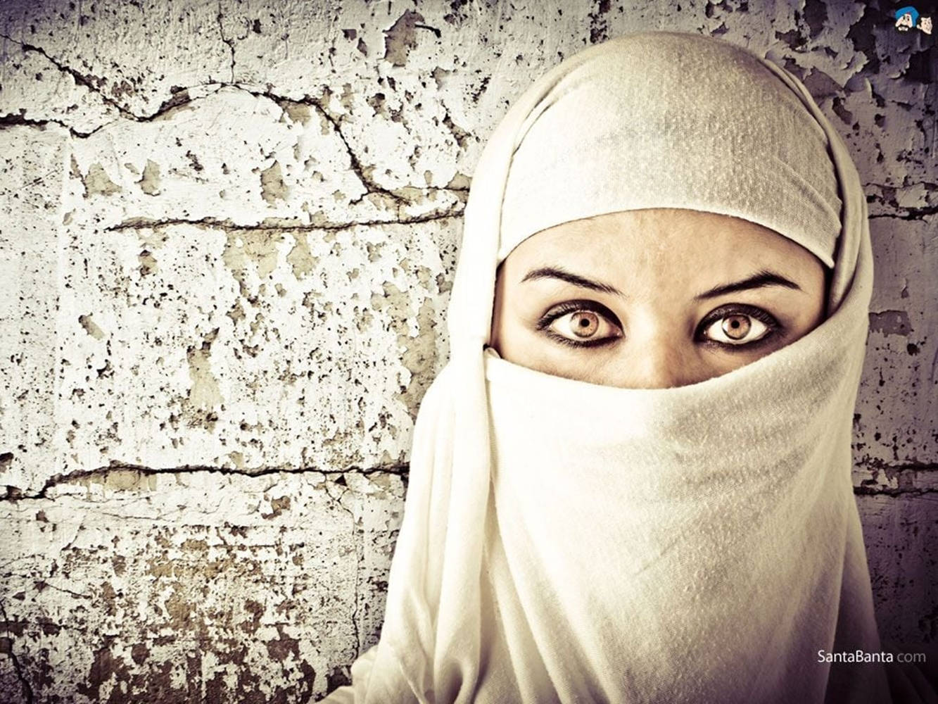 muslim 桌布 壁紙 — 一名身穿白色尼卡布的女性從一道破裂風化的牆後以令人難忘的眼神凝視。