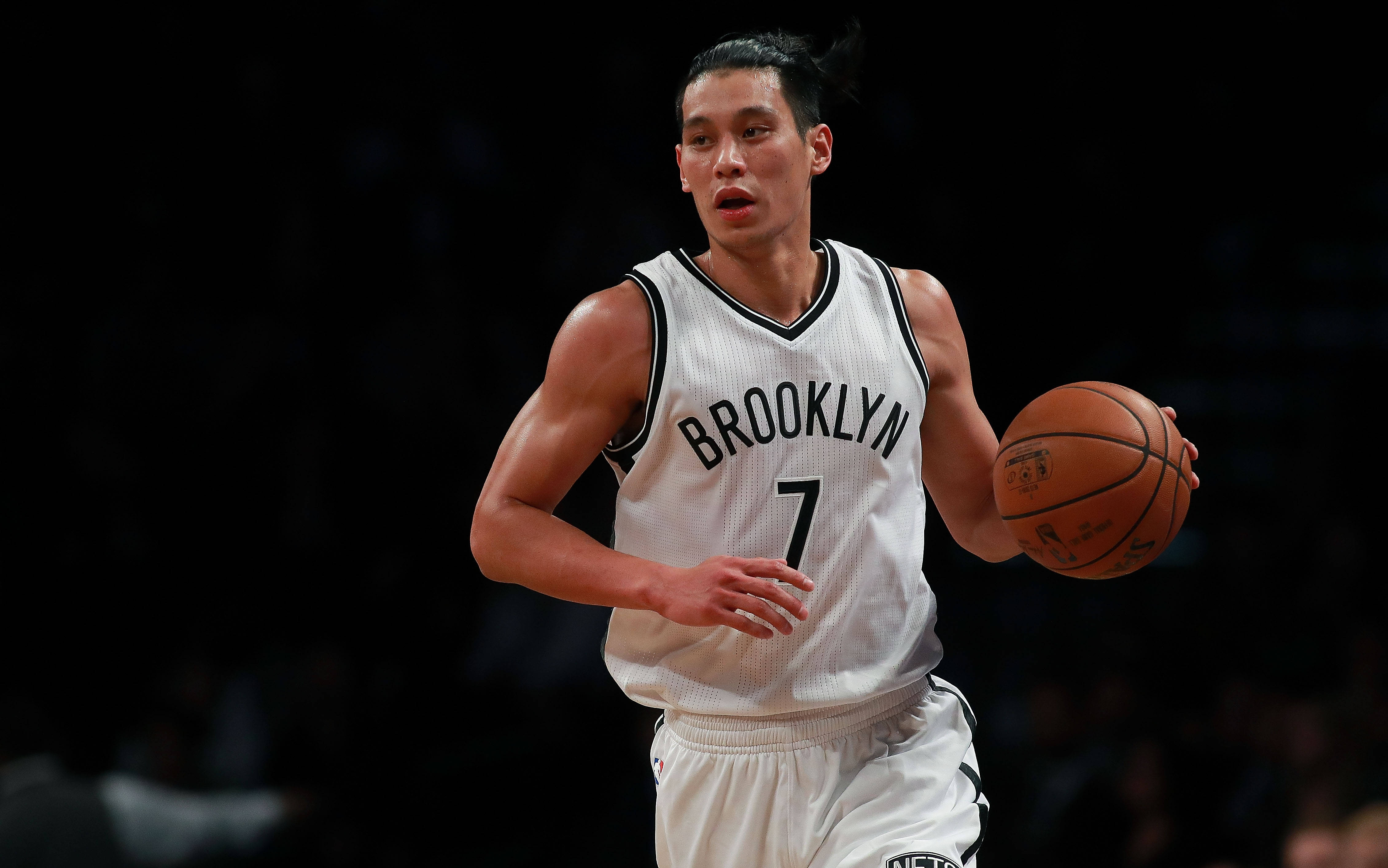 Lin 桌布 壁紙 — 一名身穿白色布魯克林球衣的籃球運動員在場館燈光下激烈運球，身後是模糊的黑暗人群。