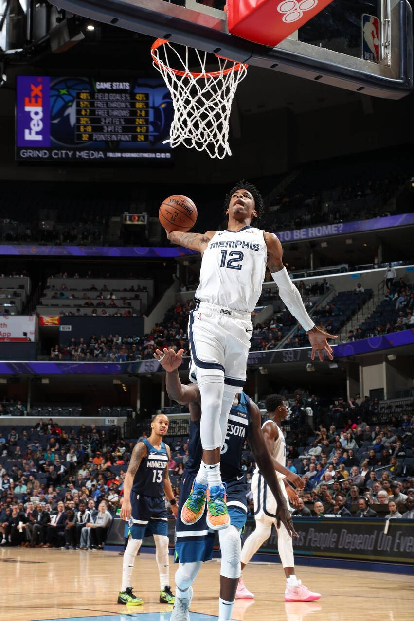 Ja Morant 灌籃 桌布 壁紙 — 一名身穿白色曼菲斯球衣的籃球運動員，在對手和座無虛席的場館觀眾注視下，專注地大力灌籃。
