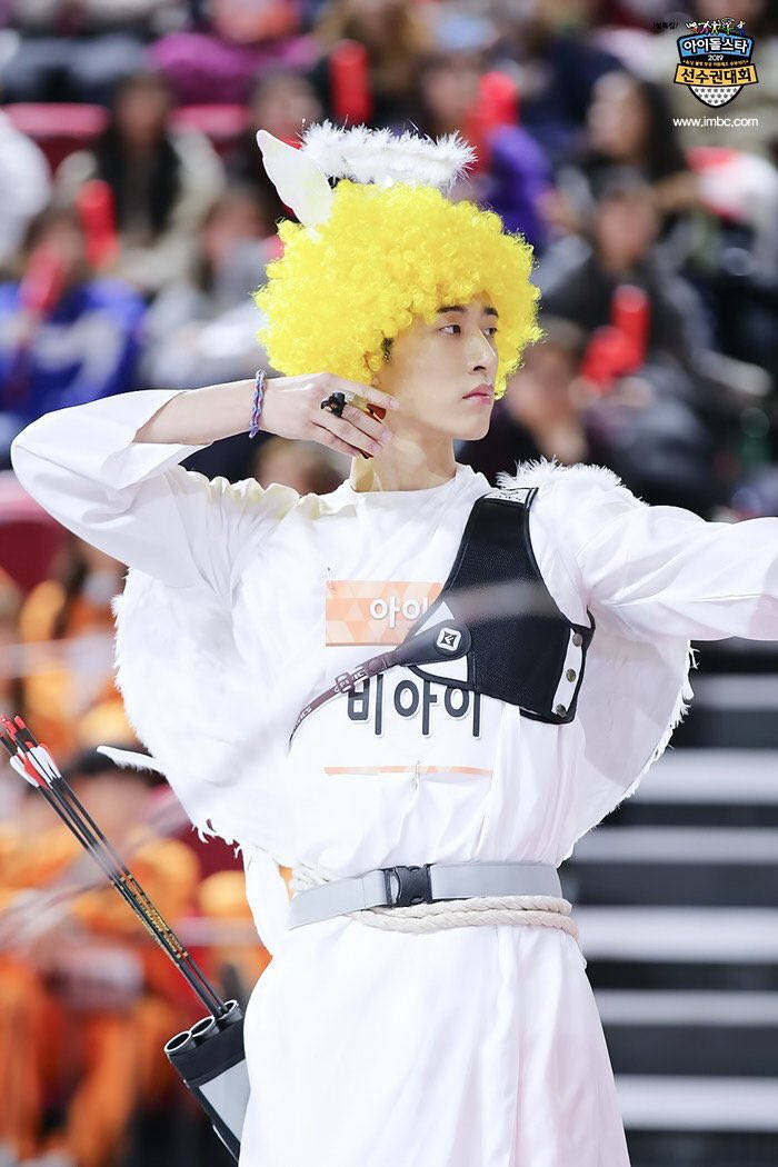 kim hanbin 桌布 壁紙 — 一名身穿白色服裝、戴著黃色假髮和狐狸耳朵的人，在電視轉播的射箭比賽中瞄準弓箭。