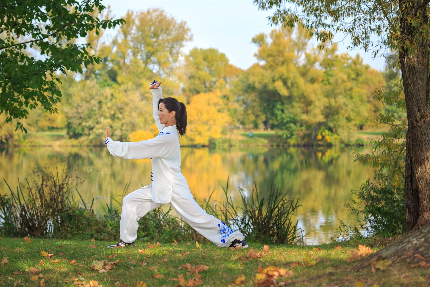 Exercise 桌布 壁紙 — 一名身穿白色武術服的女子在金黃秋葉環繞的寧靜秋湖邊優雅地練習太極拳。