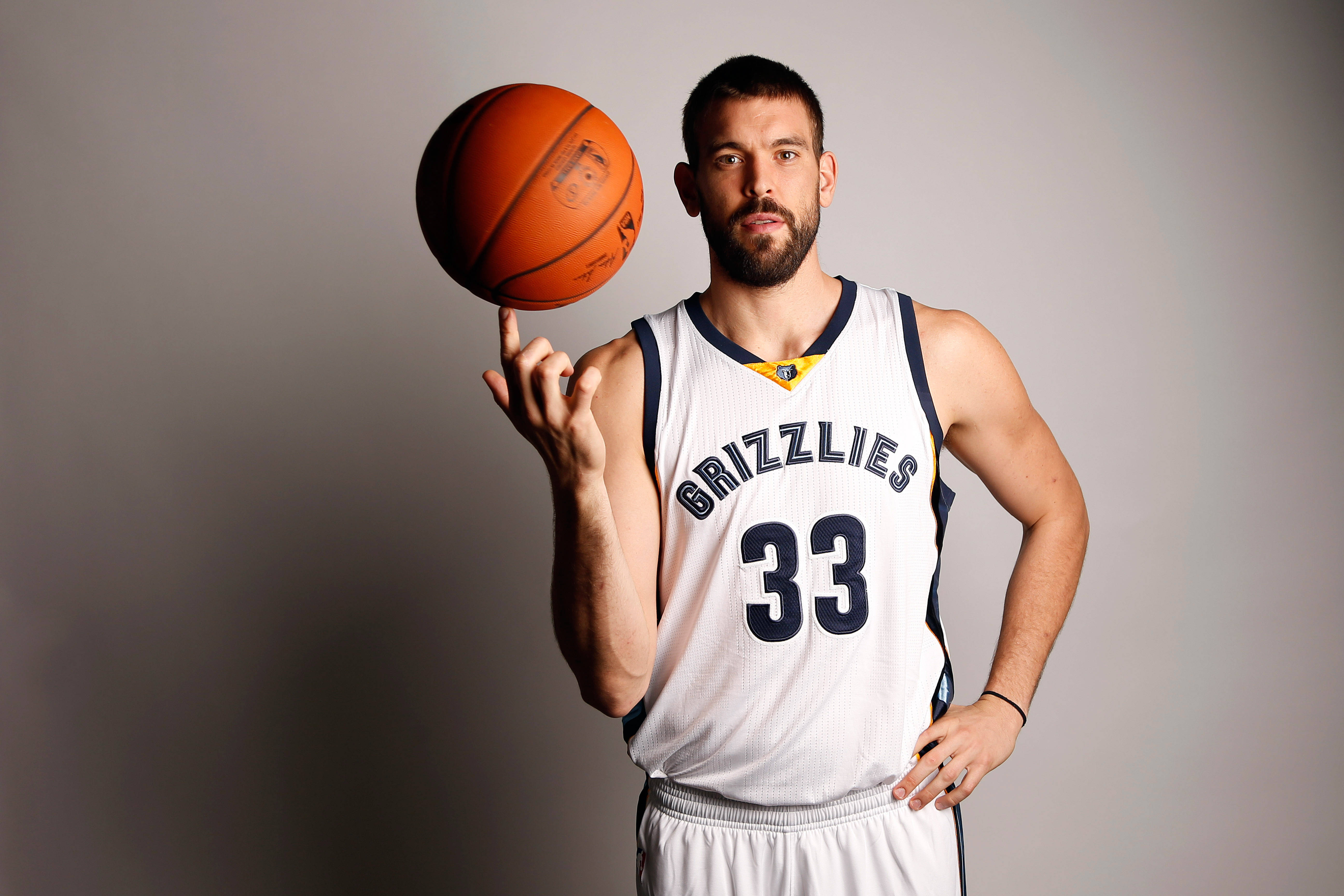 Marc Gasol 桌布 壁紙 — 一名身穿白色灰熊隊球衣的籃球運動員在純灰色工作室背景前，用指尖平衡一個橙色籃球。