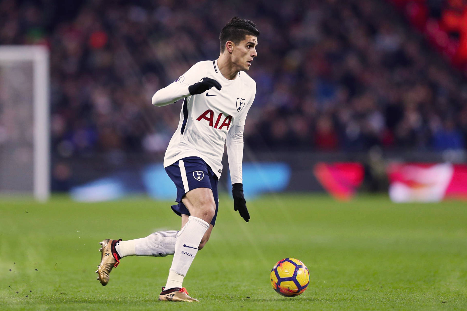 erik lamela 桌布 壁紙 — 一名身穿白色熱刺球衣的足球員在球場燈光下，於充滿活力的綠色草地上盤球。