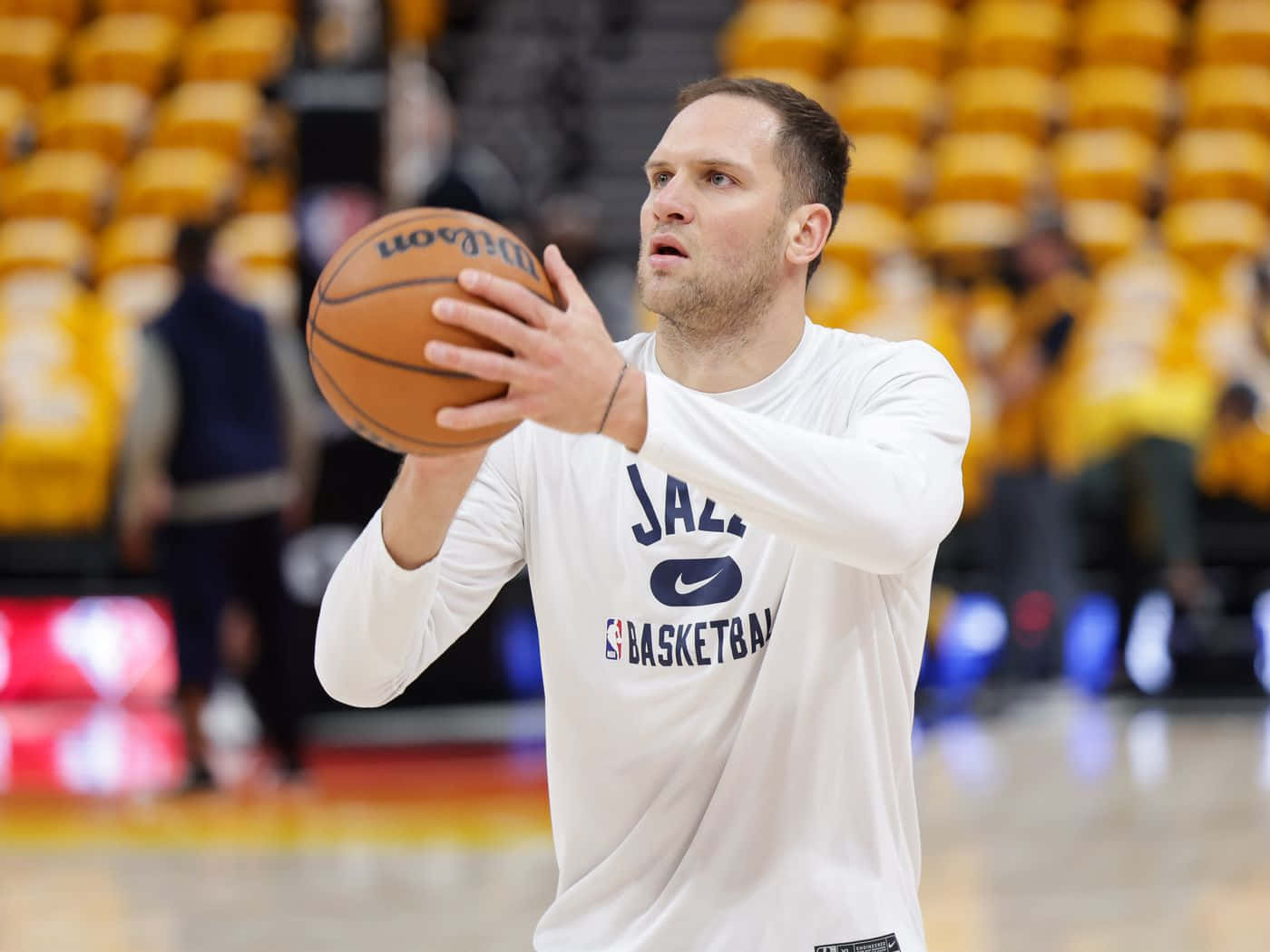 NBA 桌布 壁紙 — 一名身穿白色爵士練習球衣的籃球運動員，在一個有黃色座位的球場上準備投擲威爾遜籃球。