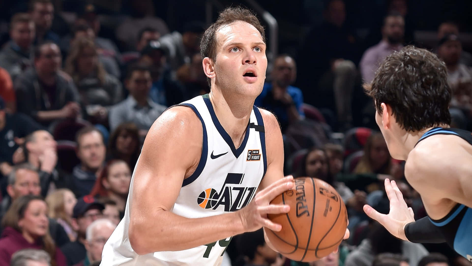 NBA 桌布 壁紙 — 一名身穿白色爵士隊球衣的籃球運動員在擠滿觀眾的場館中運球，同時被對手防守。