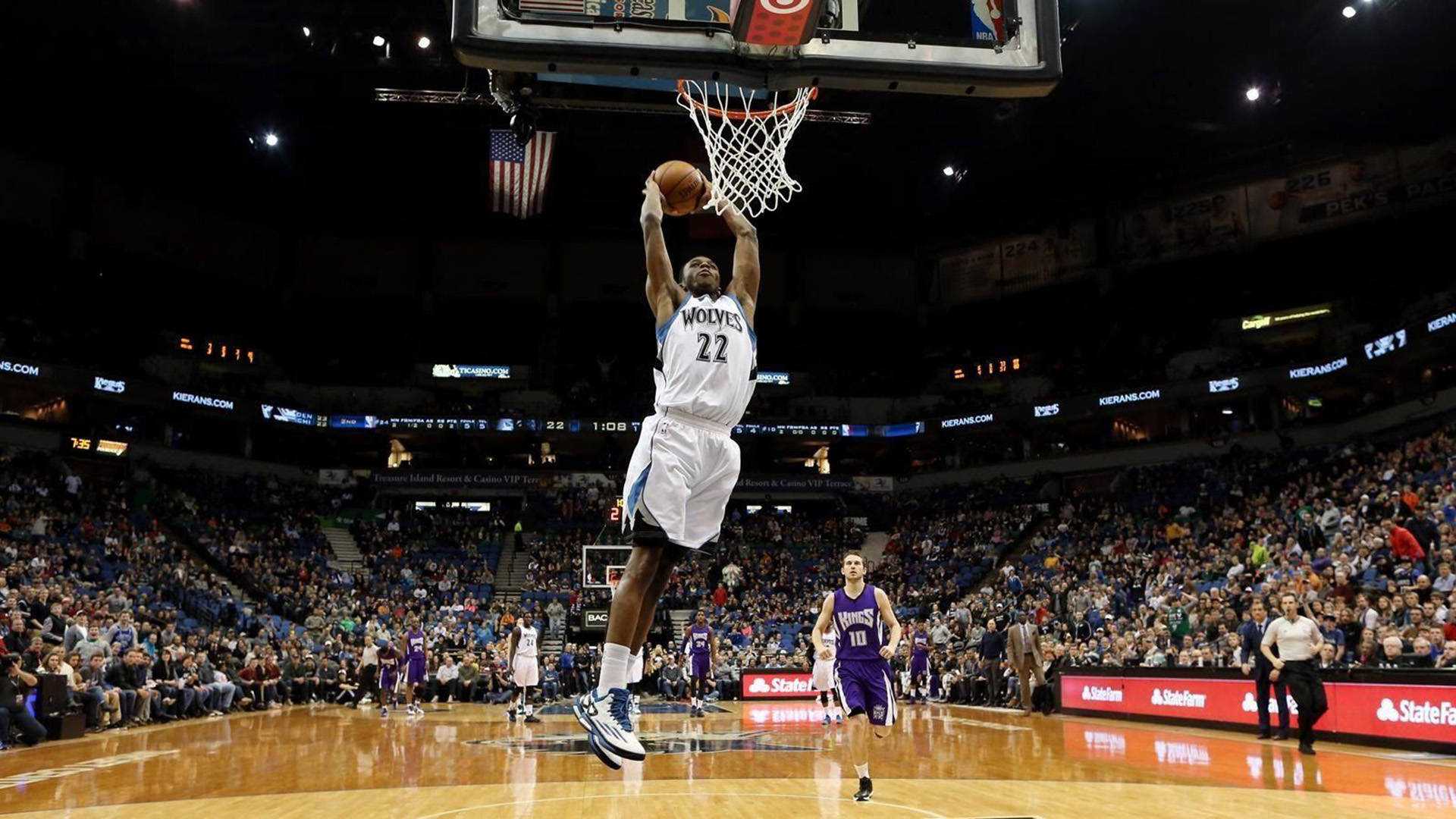 Andrew Wiggins 桌布 壁紙 — 一名身穿白色狼隊球衣的籃球運動員在明亮的場館燈光下，在座無虛席的場館中灌籃。