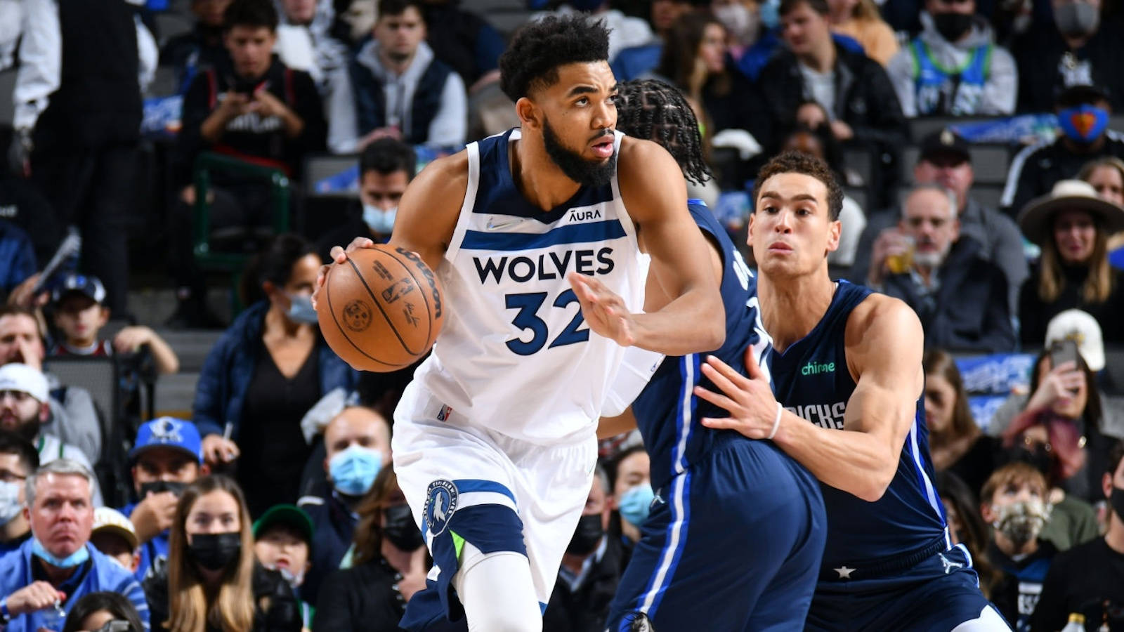 karl-anthony towns 桌布 壁紙 — 一名身穿白色狼隊球衣的籃球運動員在現場比賽中運球，同時被一名身穿藍色球衣的對手緊密防守。