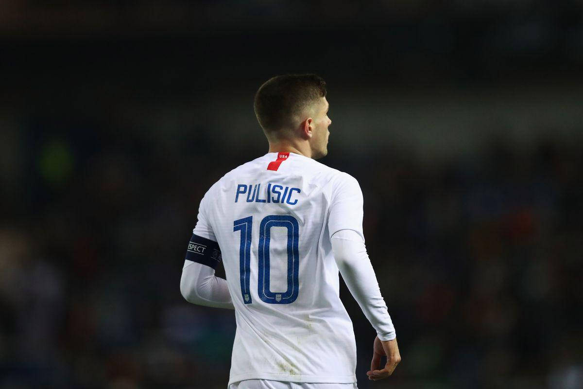 christian pulisic 桌布 壁紙 — 一名身穿白色球衣、印有普利西奇名字和10號的足球員背對鏡頭站在昏暗的球場上。