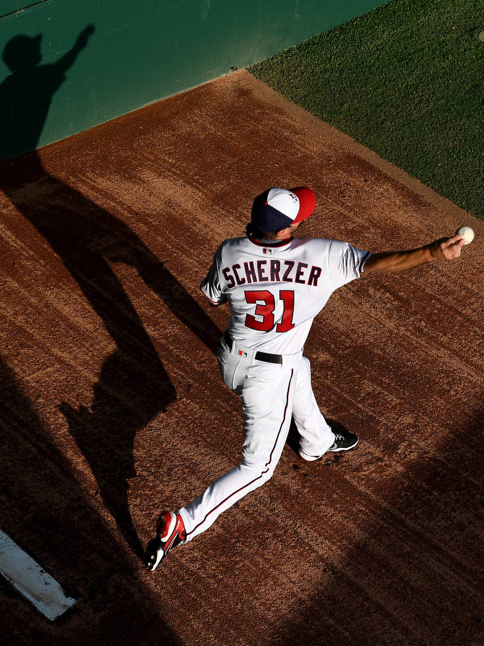 Max Scherzer 桌布 壁紙 — 一名身穿白色球衣、紅色31號的棒球投手，在明亮的陽光下從泥土投手丘上投球，投出長長的影子。