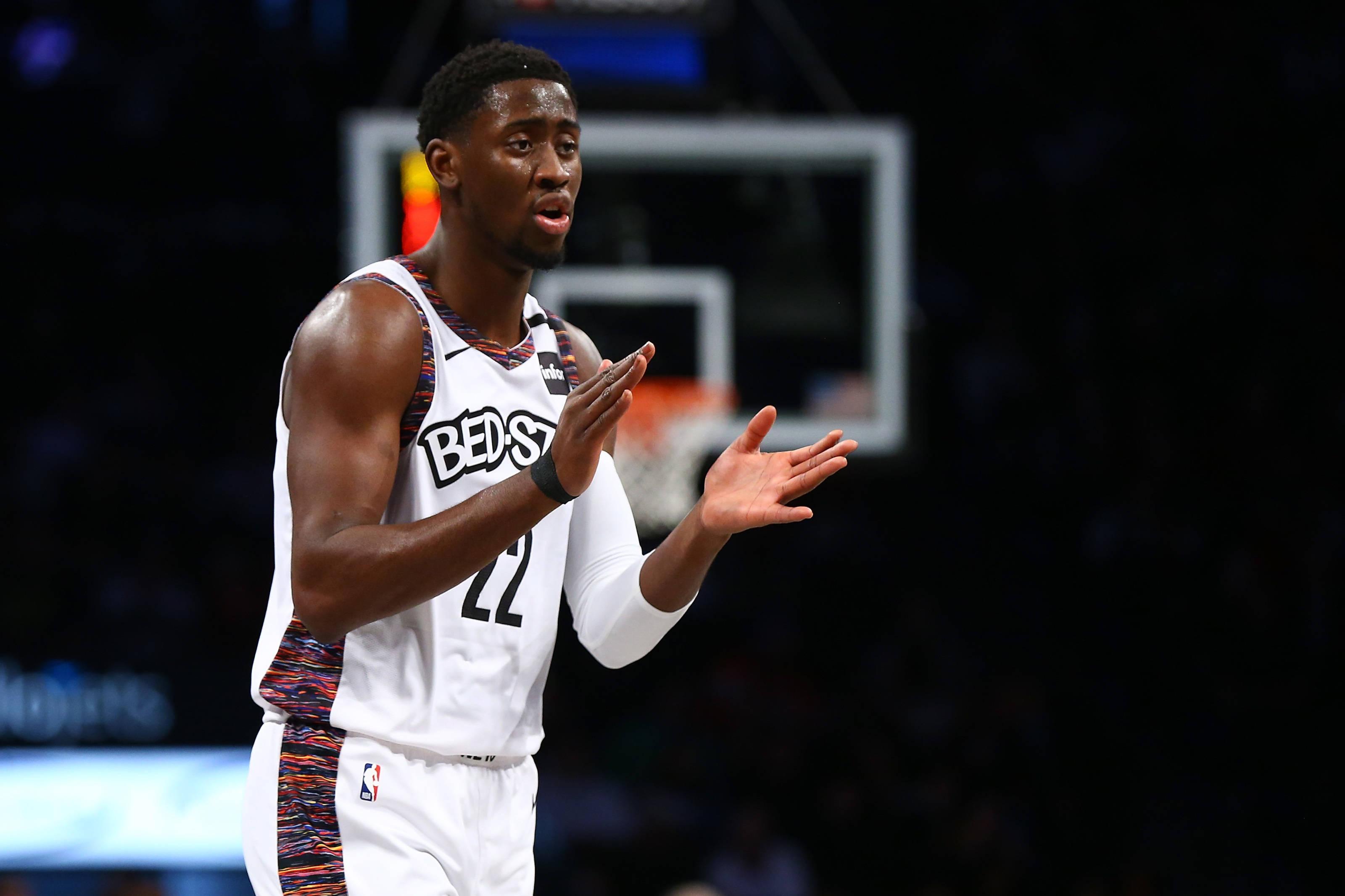 caris levert 桌布 壁紙 — 一名身穿白色球衣、背號22的籃球運動員在場館燈光下比賽時張開雙手做手勢。