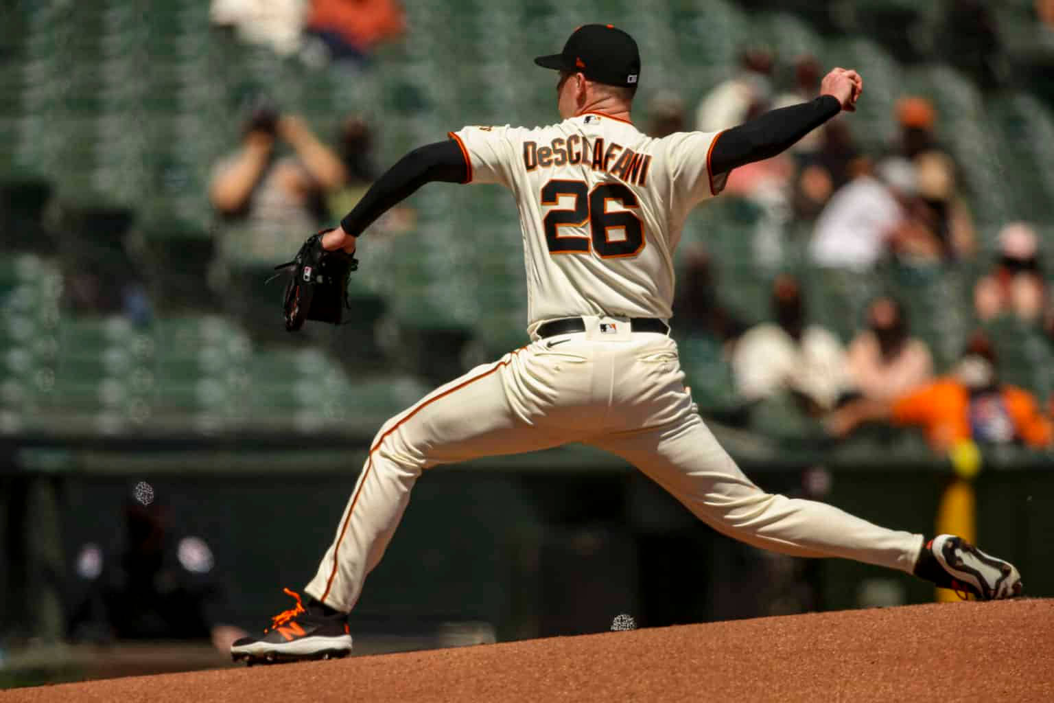 運動 桌布 壁紙 — 一名身穿白色球衣、背號26的棒球投手，在陽光普照的投手丘上投球，背景有模糊的觀眾。