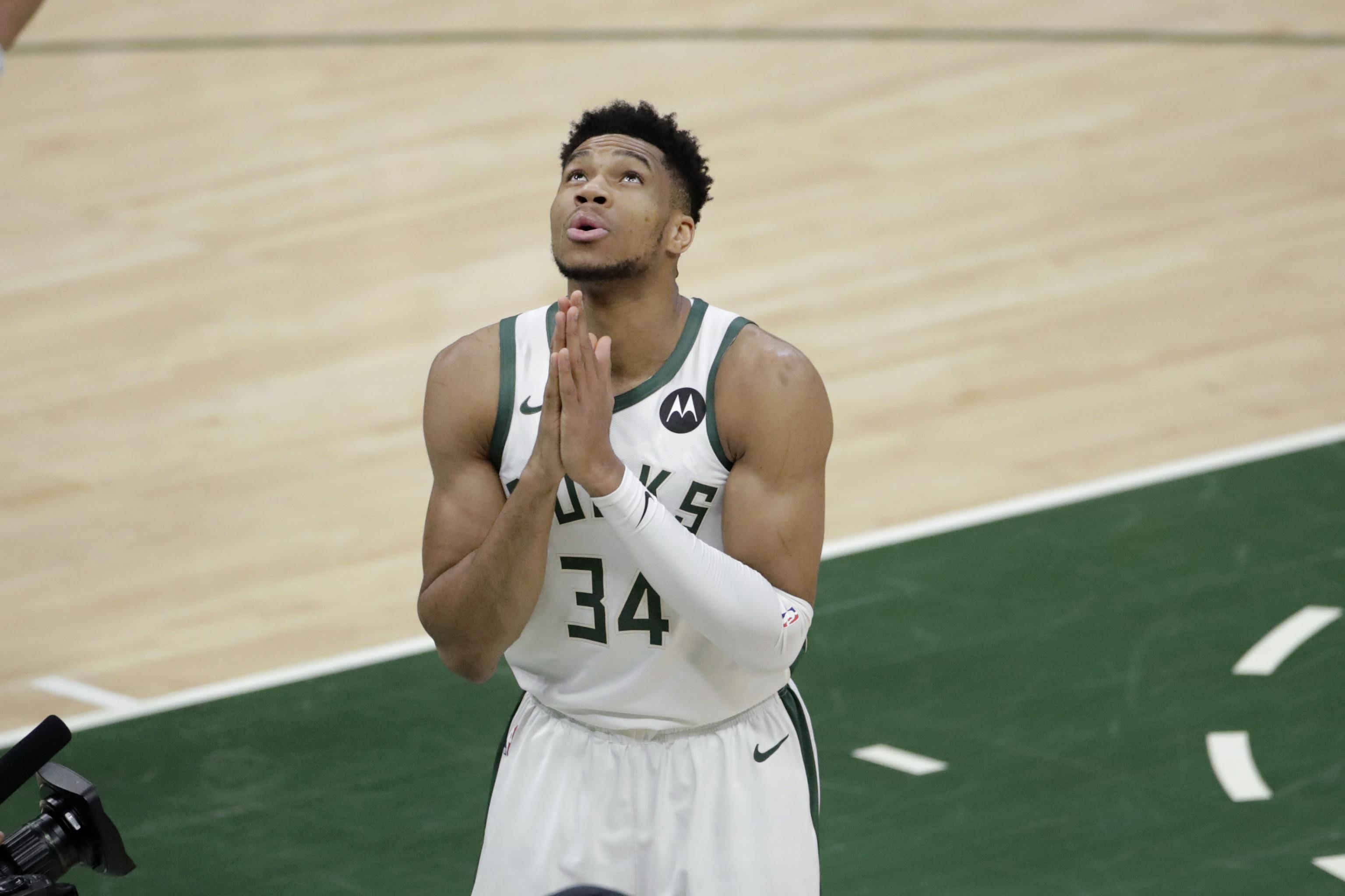 Giannis 桌布 壁紙 — 一名身穿白色球衣、背號34的籃球運動員在球場上合十祈禱。