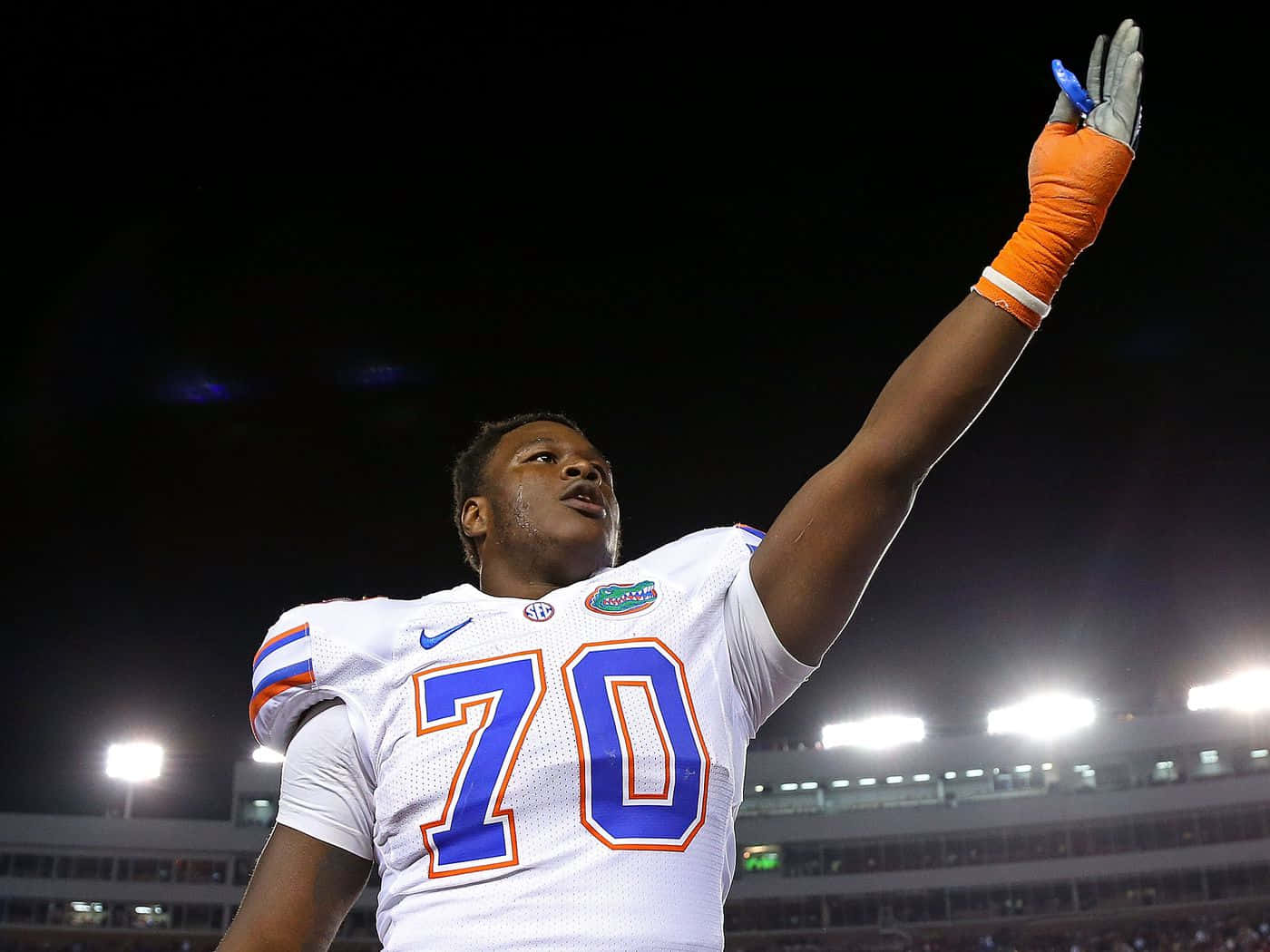 Florida Gators 桌布 壁紙 — 一名身穿白色球衣、號碼70的美式足球員在夜間球場燈光下舉起戴著手套的手慶祝勝利。