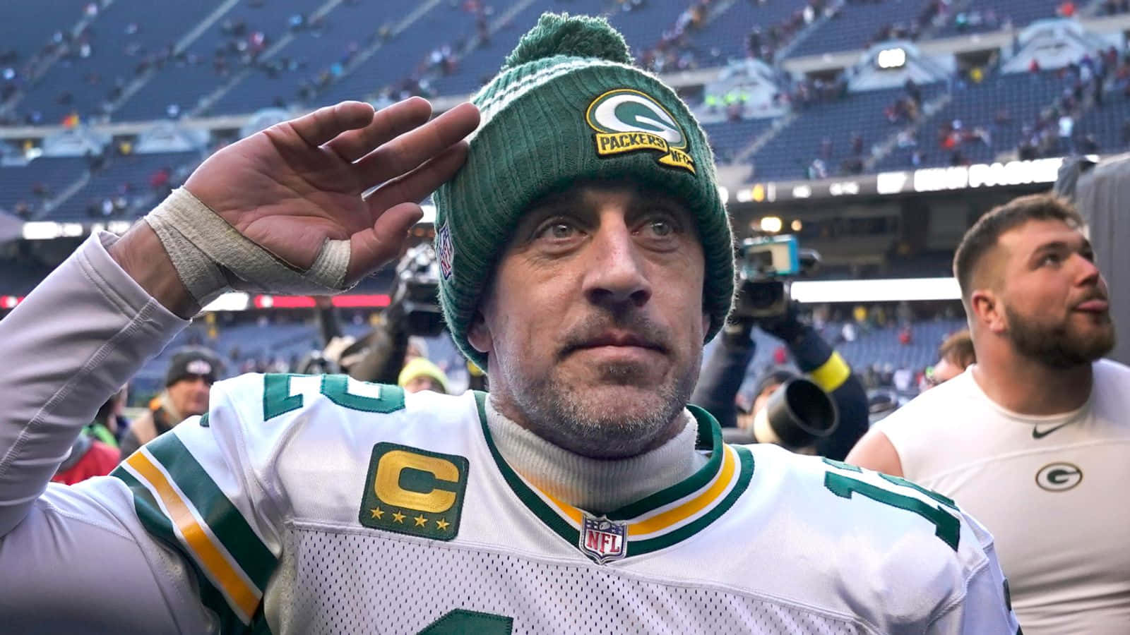 Aaron Rodgers 桌布 壁紙 — 一名身穿白色球衣和綠色毛帽的綠灣包裝工球員在擠滿觀眾的體育館向球迷致敬。